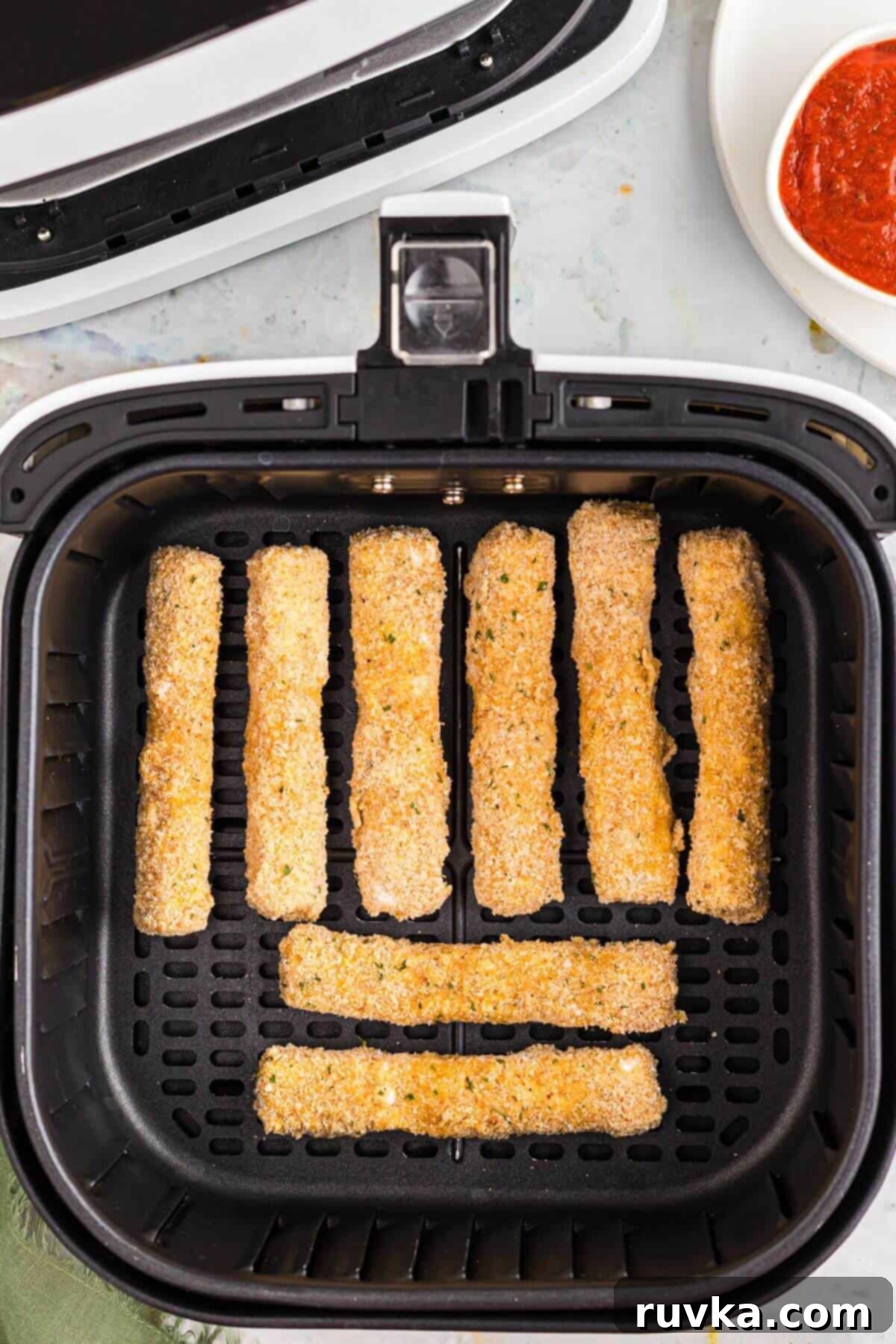 Crispy Air Fryer Mozzarella Sticks 6 Breaded mozzarella cheese sticks in the air fryer basket before being air fried.