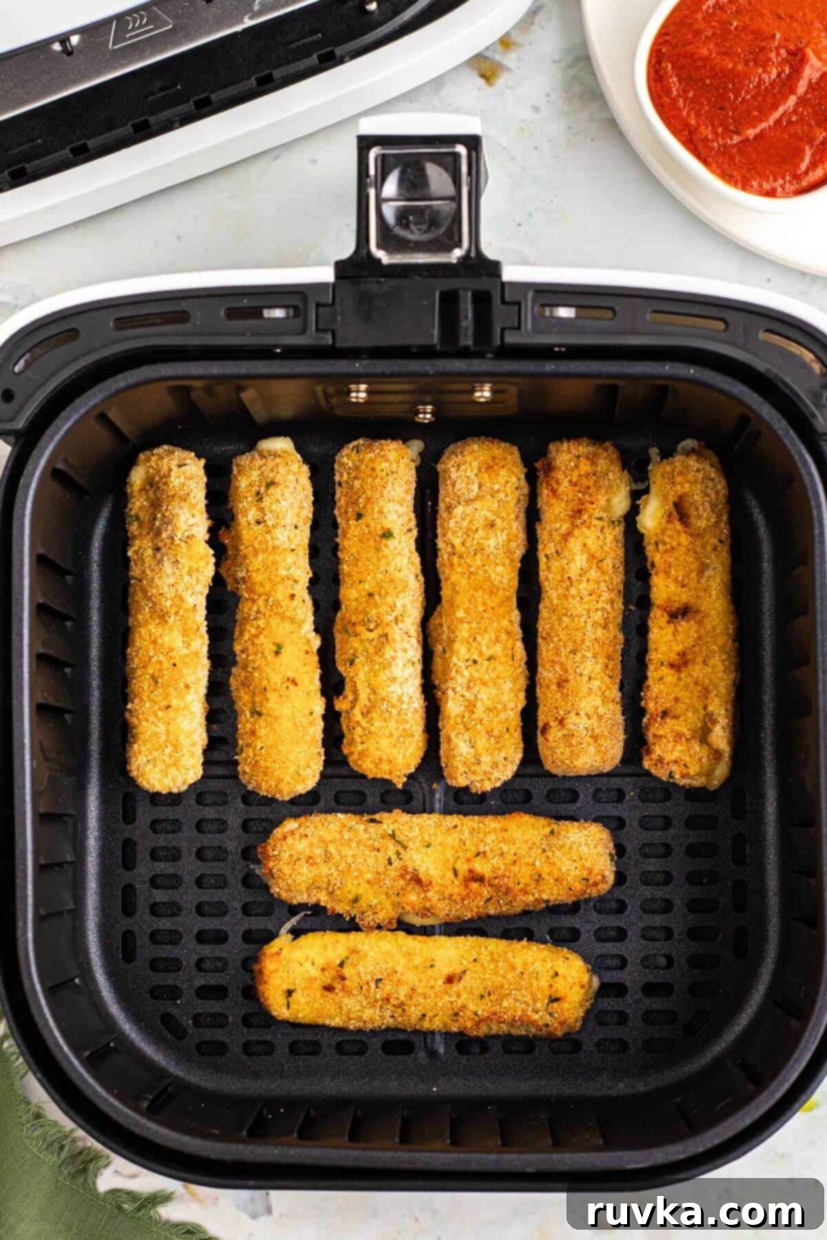 Crispy Air Fryer Mozzarella Sticks 7 Golden brown breaded mozzarella sticks in the air fryer basket after being air fried.
