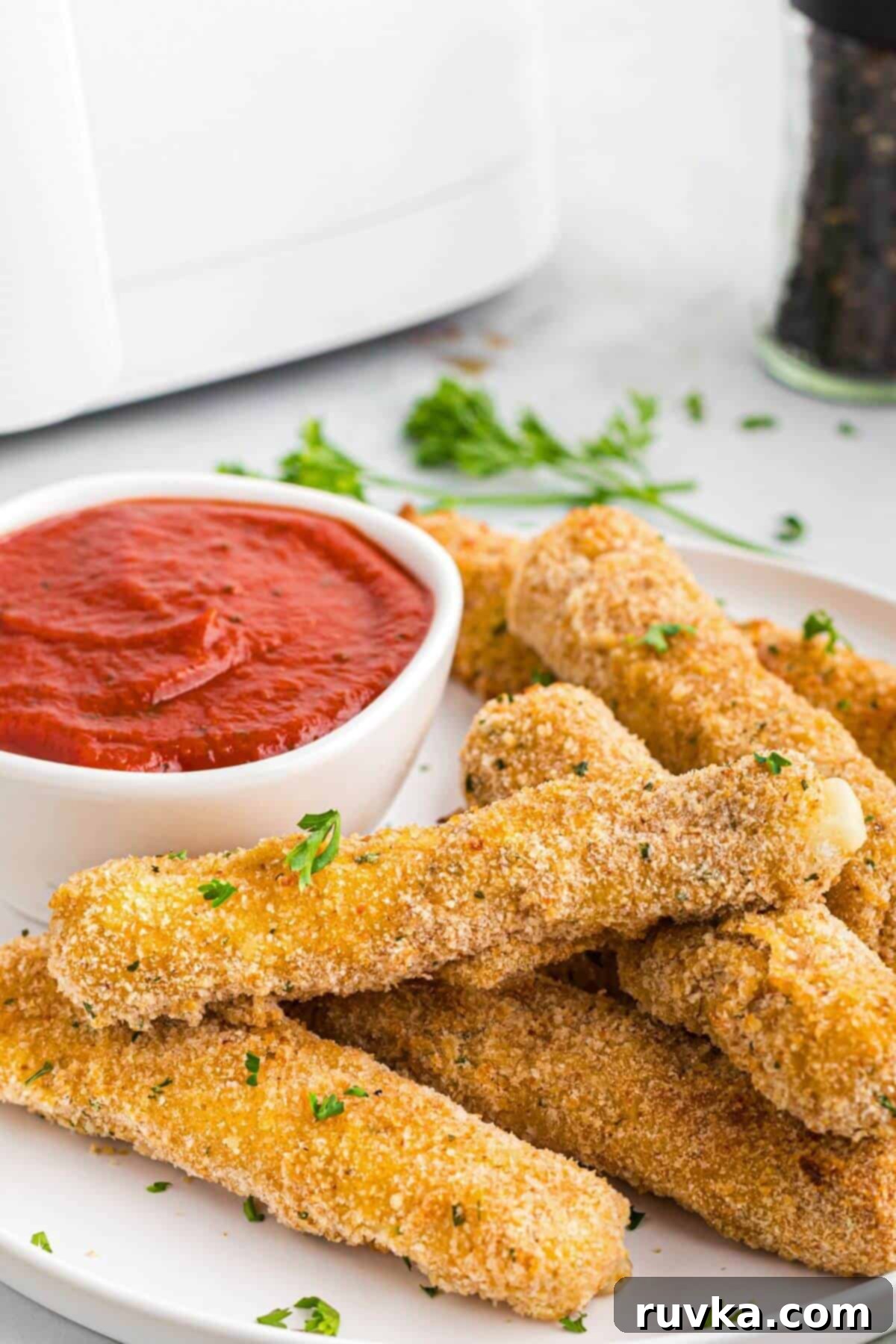Crispy Air Fryer Mozzarella Sticks 8 Golden crispy breaded cheese sticks stacked on a white plate with warm marinara sauce.