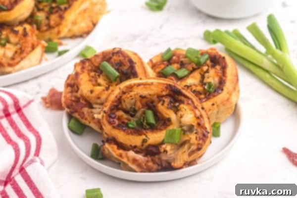 Crispy Air Fryer BBQ Chicken Pizza Rolls 2 Golden bbq rolls with chicken and sauce, topped with chopped green onions on a white plate.