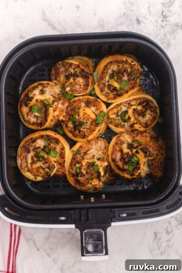 Crispy Air Fryer BBQ Chicken Pizza Rolls 7 Cooked air fryer BBQ chicken pizza roles in the air fryer basket, sprinkled with chopped green onions.