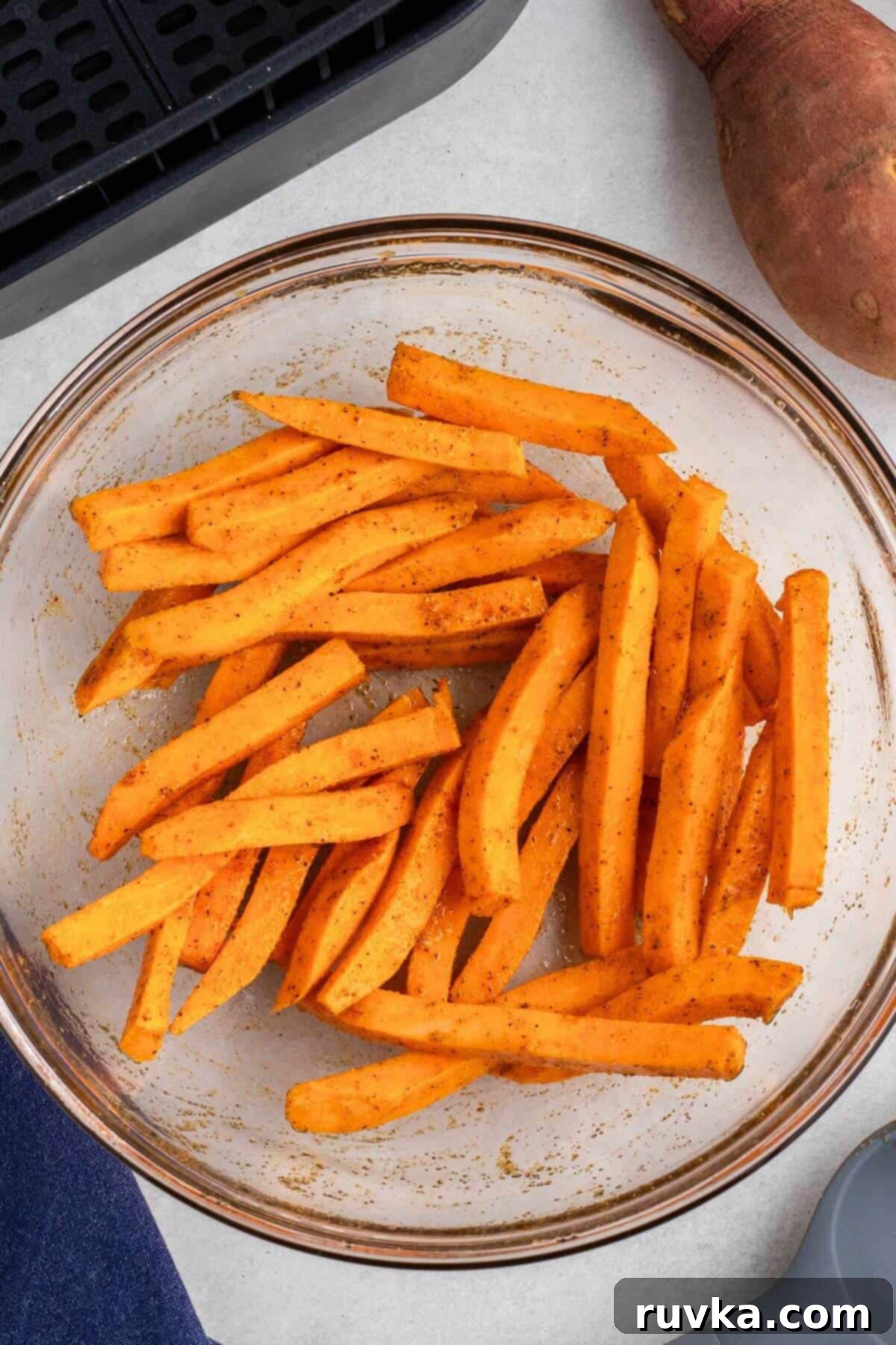 Crispy Air Fryer Sweet Potato Fries 5 Sweet potatoes cut into strips and tossed with olive oil and seasonings in a clear glass bowl.