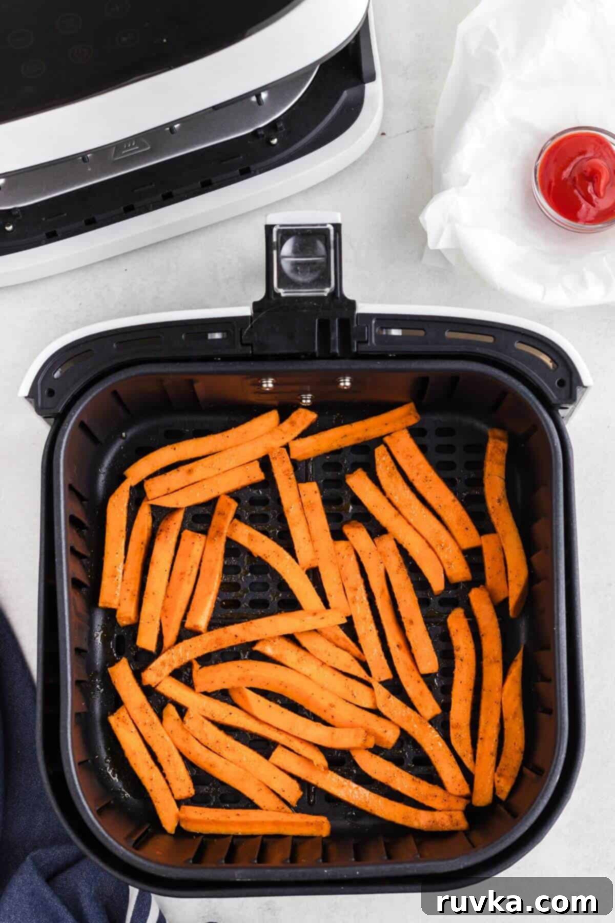 Crispy Air Fryer Sweet Potato Fries 6 Uncooked seasoned sweet potatoes cut into strips, in the air fryer basket.