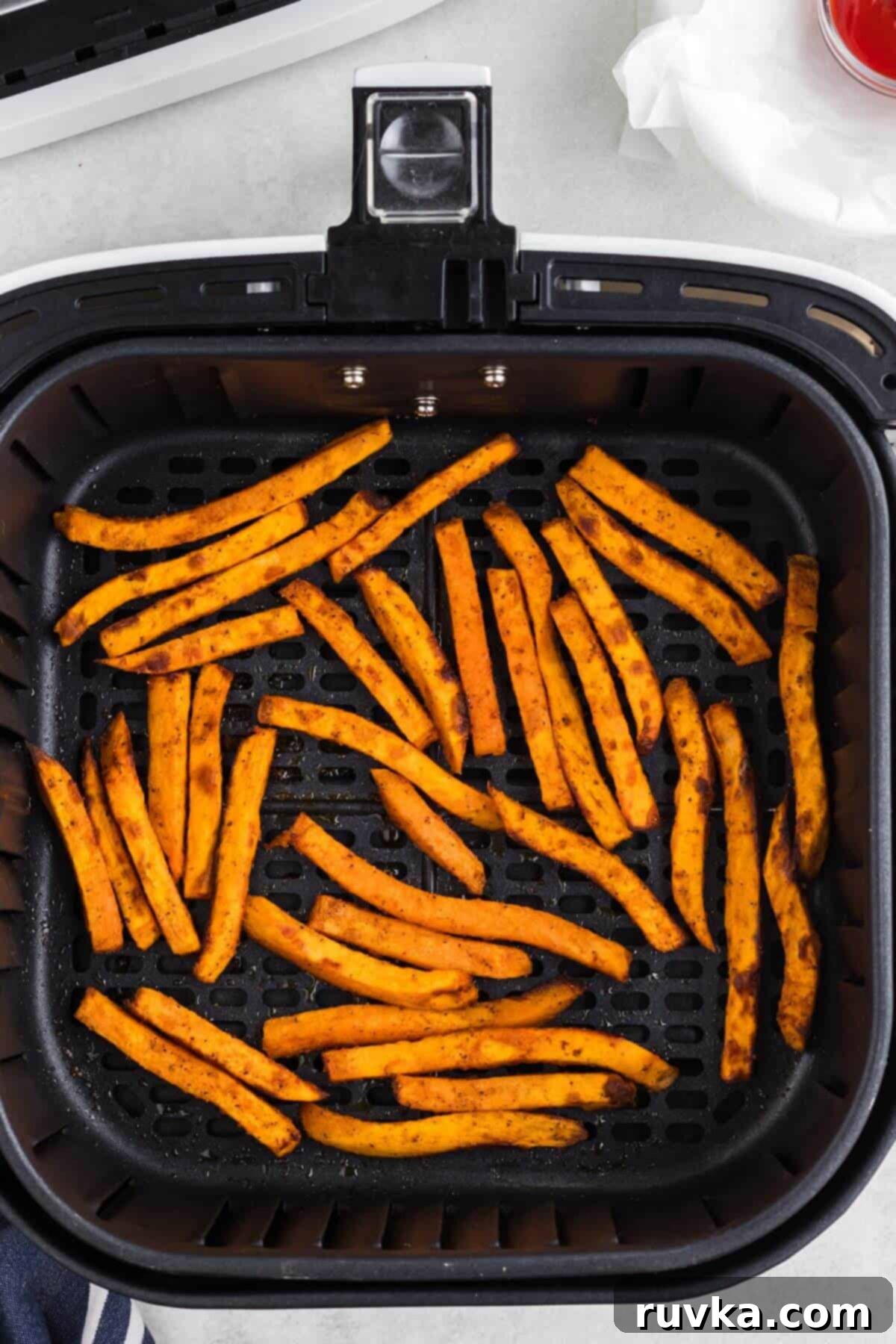 Crispy Air Fryer Sweet Potato Fries 7 Seasoned sweet potato fries in the air fryer basket after being cooked.