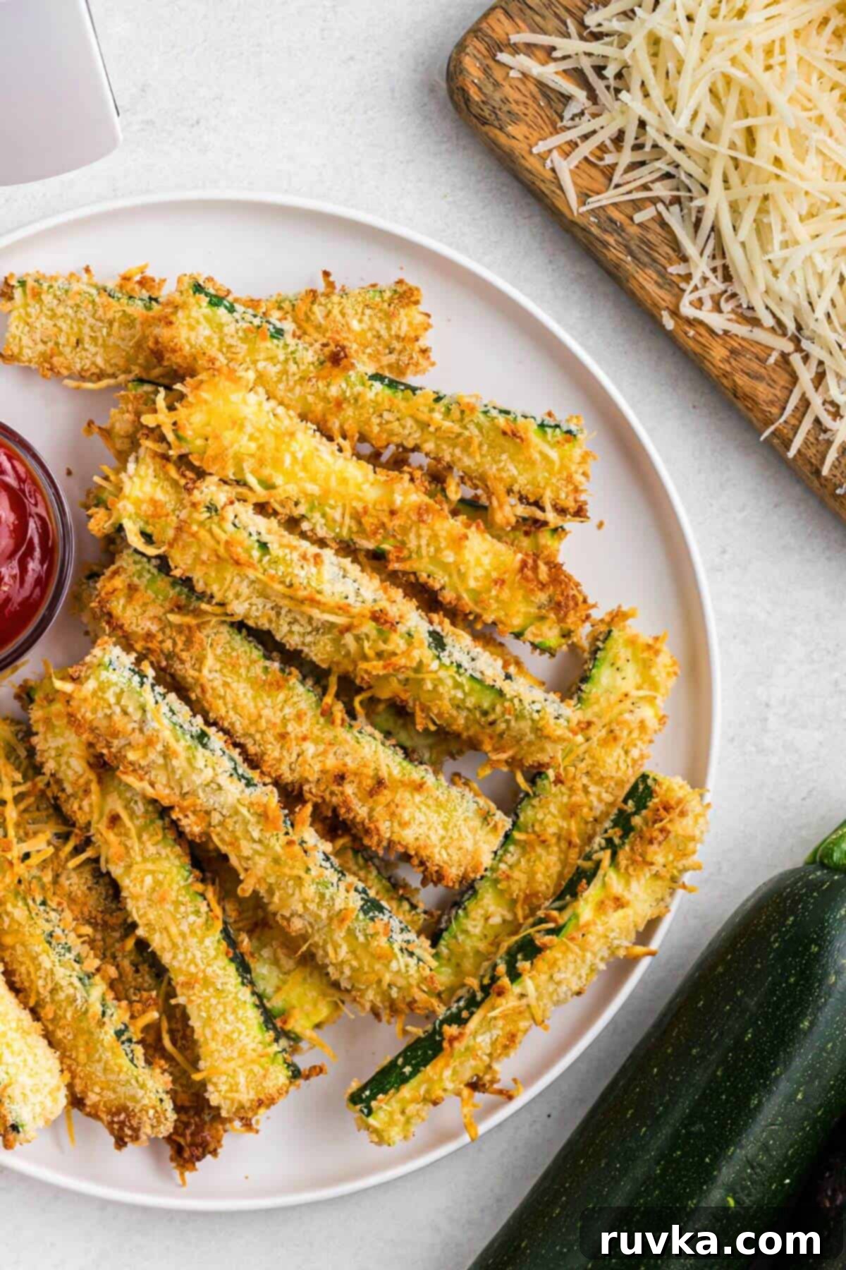 Guilt-Free Air Fryer Zucchini Fries 2 Golden crusted zucchini fries stacked on a white plate in front of the air fryer.