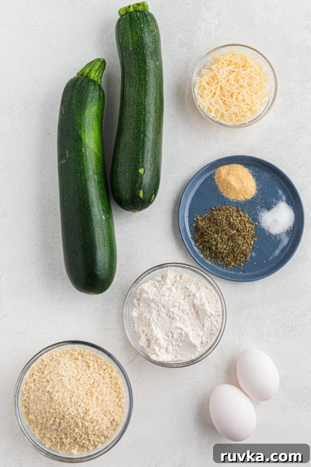 Guilt-Free Air Fryer Zucchini Fries 3 Zucchini, breadcrumbs, parmesan cheese, flour, eggs, and seasonings measured on a white marble table.