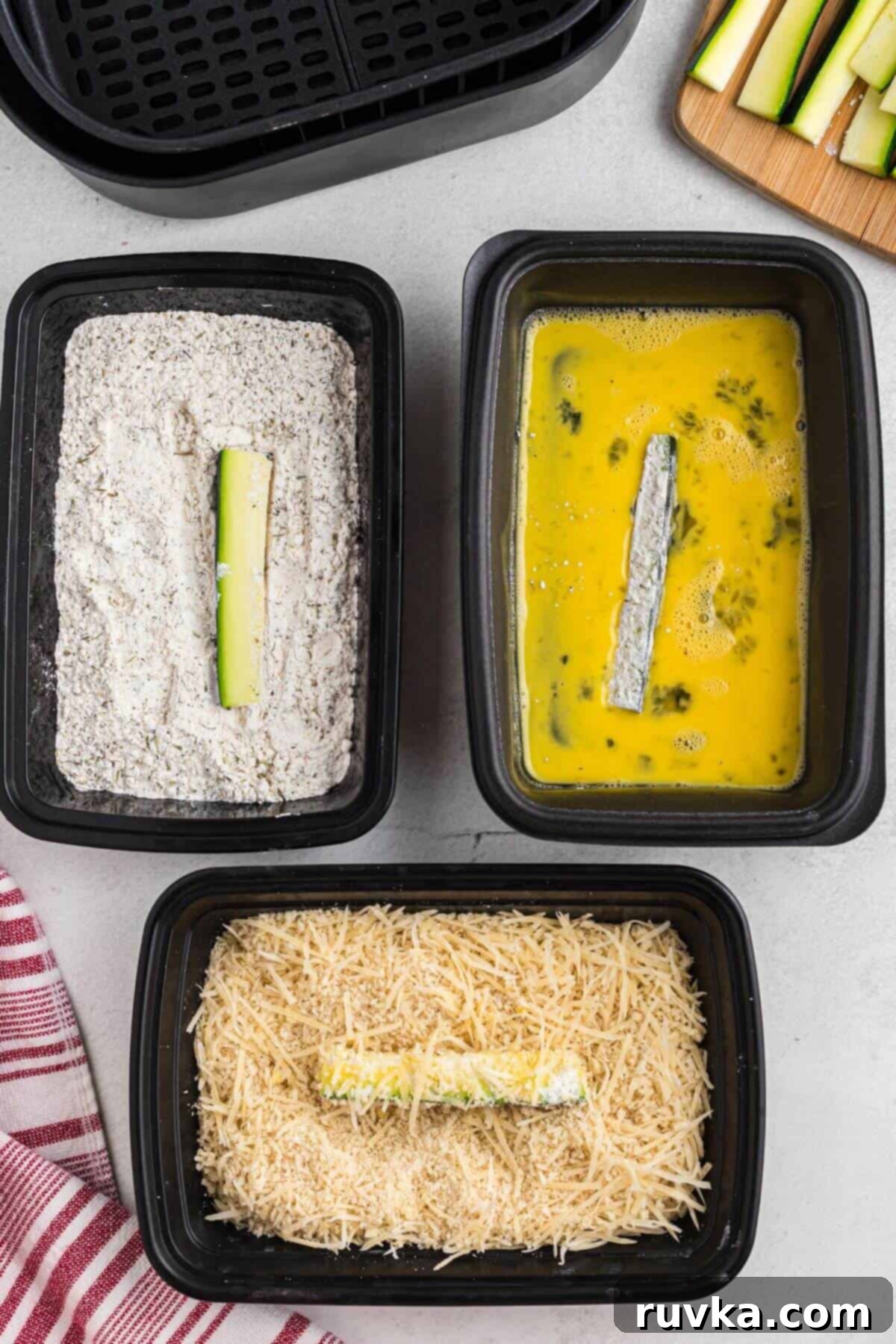 Guilt-Free Air Fryer Zucchini Fries 5 Zucchini sticks being dipped in flour, then egg, than parmesan cheese and bread crumbs.