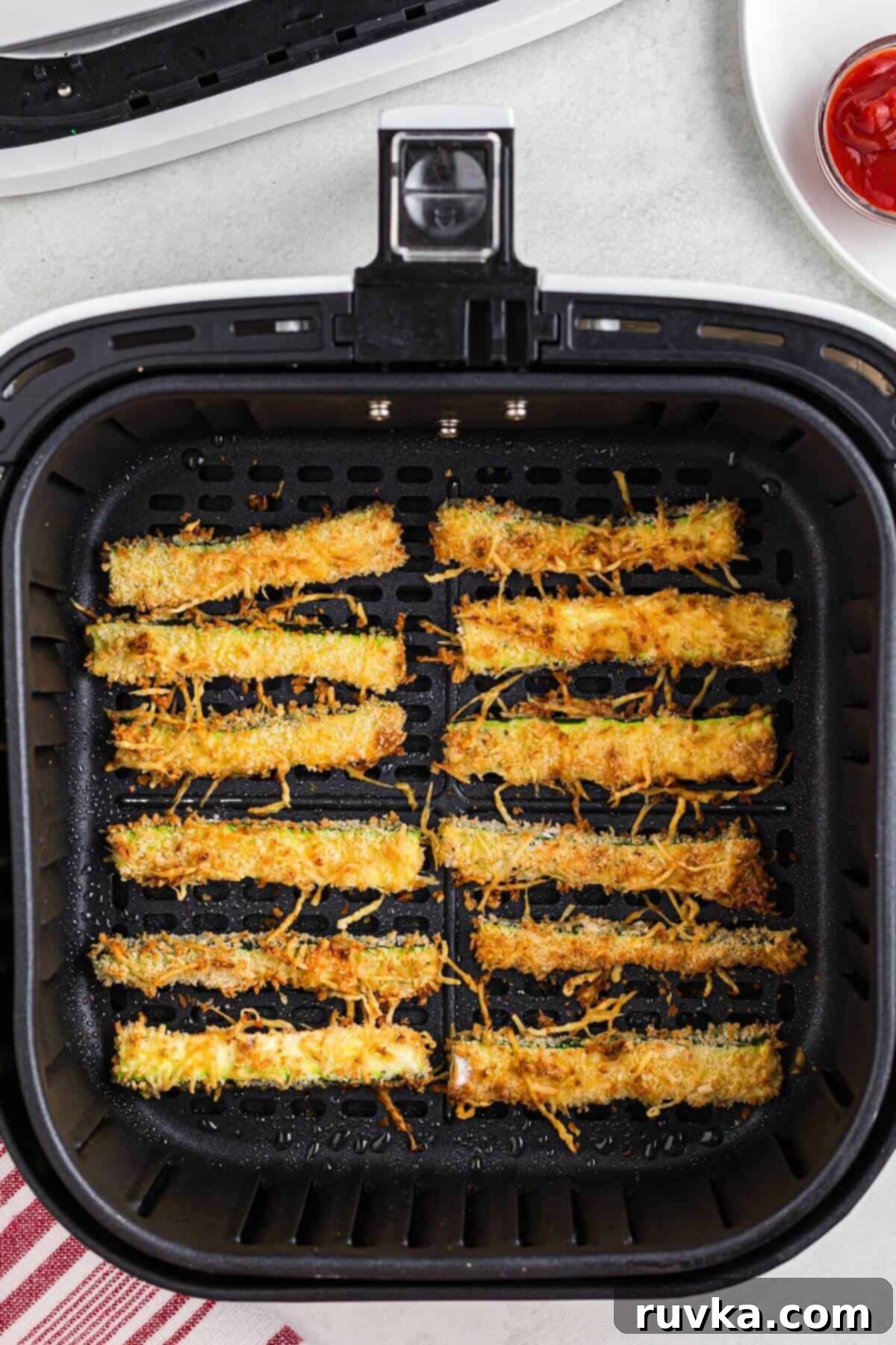Guilt-Free Air Fryer Zucchini Fries 7 Crispy golden brown cheesy zucchini fries in the air fryer basket after being cooked.