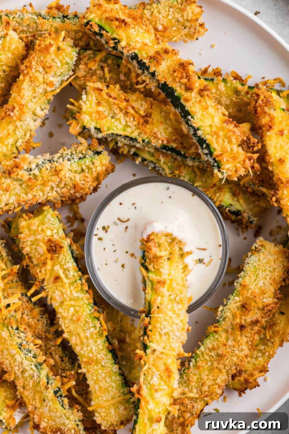 Guilt-Free Air Fryer Zucchini Fries 8 Golden crispy zucchini fries on a white plate with one fry in ranch dressing.