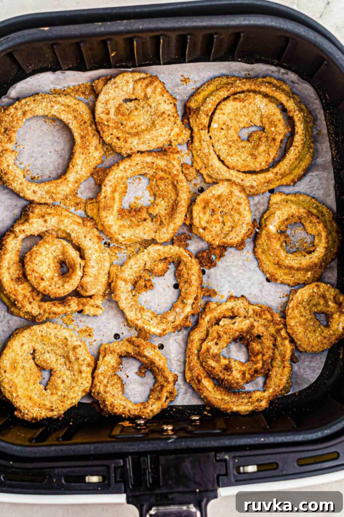 Bring Back the Crunch Air Frying Onion Rings 3 Onion rings being reheated in the air fryer basket on top of a piece of parchment paper that's being used for easier cleanup.