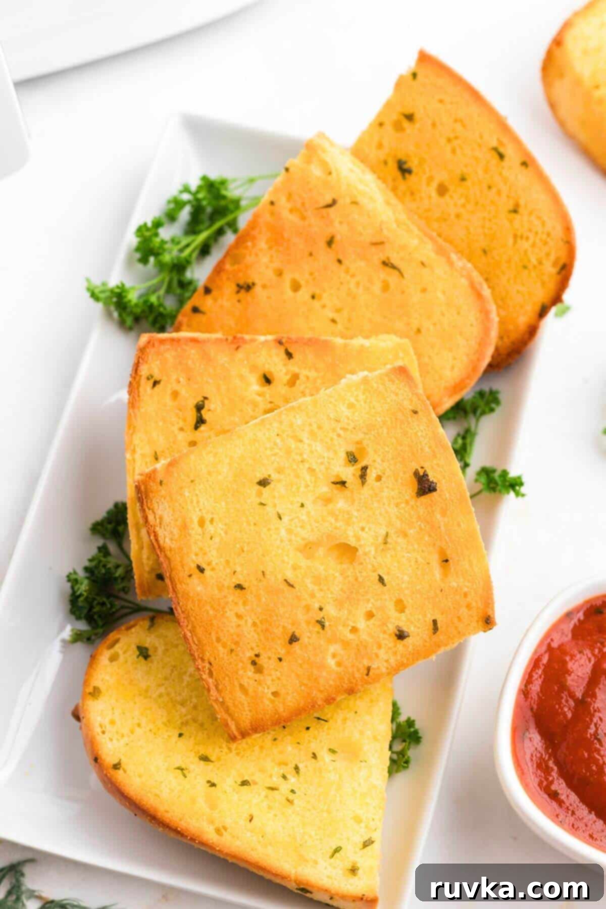 Perfect Air Fryer Frozen Garlic Bread 2 Golden crispy garlic bread on a white plate with marinara sauce on the side.