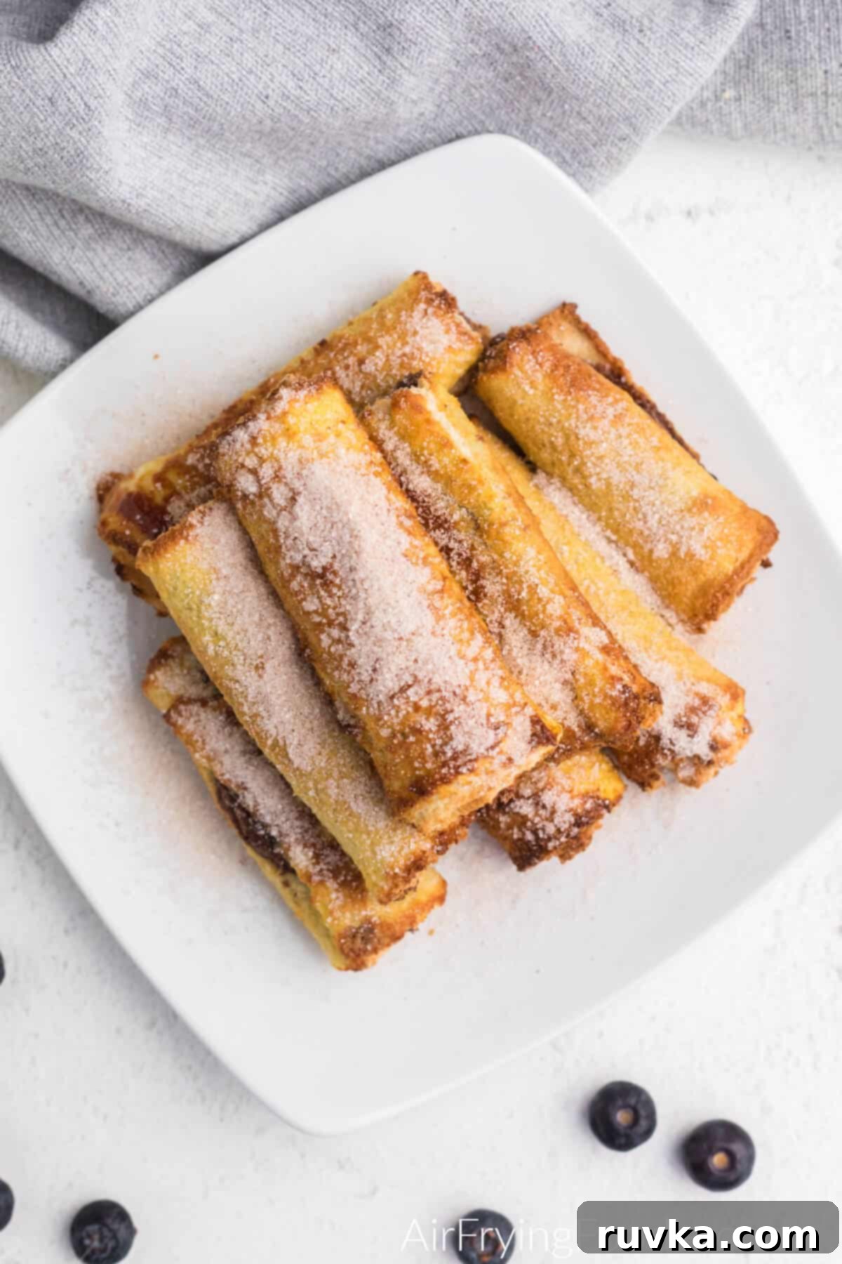 Nutella Stuffed Air Fryer French Toast Pinwheels 6 Overhead photo of air fryer nutella french toast rolls ups on a plate with cinnamon and sugar sprinkled on top.