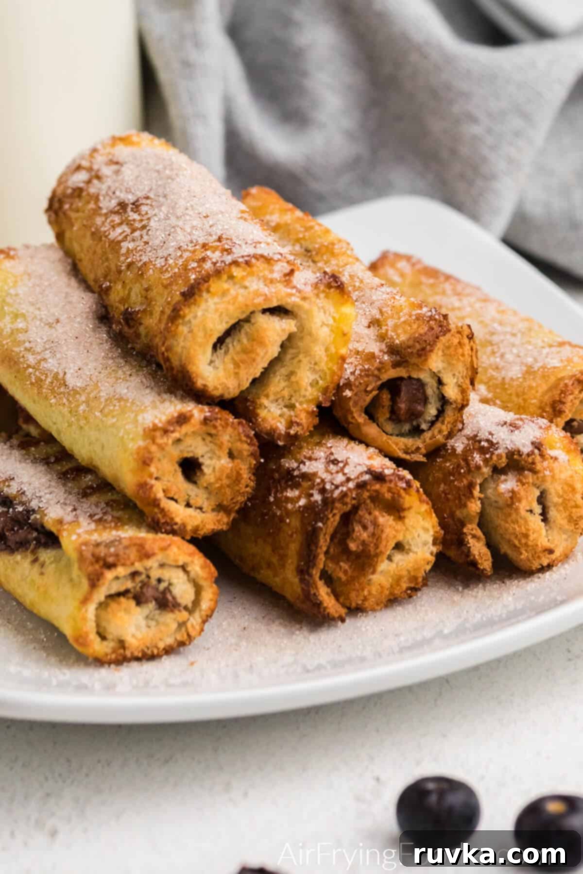 Nutella Stuffed Air Fryer French Toast Pinwheels 7 air fryer nutella french toast roll ups on a white olate topped with cinnamon and sugar.
