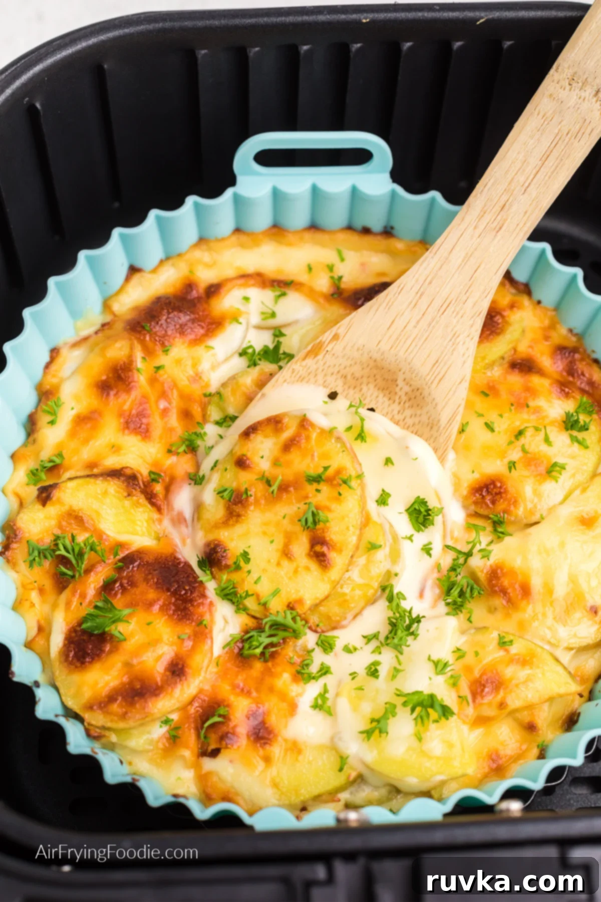 Reusable Air Fryer Silicone Baskets 2 Air fryer scalloped potatoes topped with fresh parsley and a wooden spoon scooping out a serving from a silicone liner.