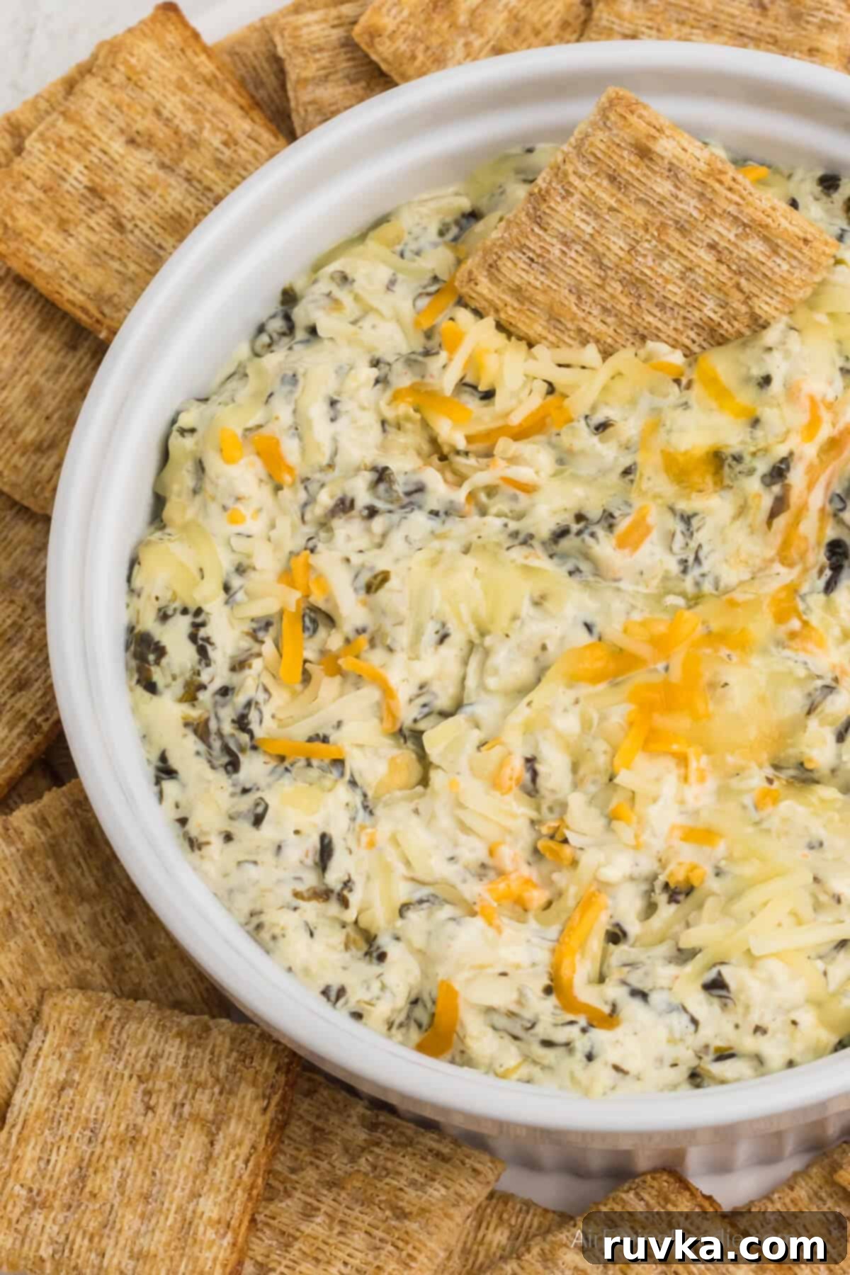 Easy Air Fryer Artichoke Spinach Dip 2 Artichoke spinach dip in an air fryer safe dish, surrounded by Triscuit crackers for dipping.