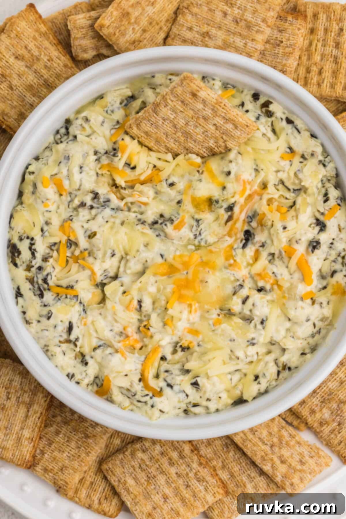 Easy Air Fryer Artichoke Spinach Dip 5 Air fried artichoke spinach dip in a round white dish, surrounded by Triscuit chips for serving.