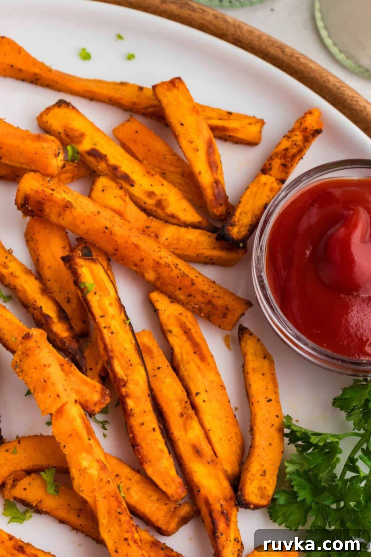 Effortless Holiday Feasts: 15 Air Fryer Recipes 5 Sweet potato fries on a round white plate with ketchup and parsley.