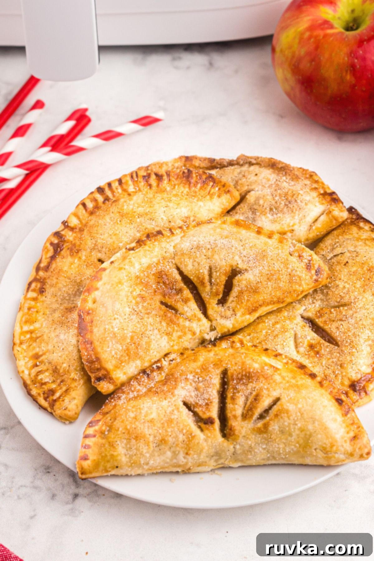 Sizzle into the New Year: 15 Air Fryer Recipes to Revolutionize Your Cooking 17 Apple hand pies on a white plate with red and white straws and an apple on the table off to the back of the plate.