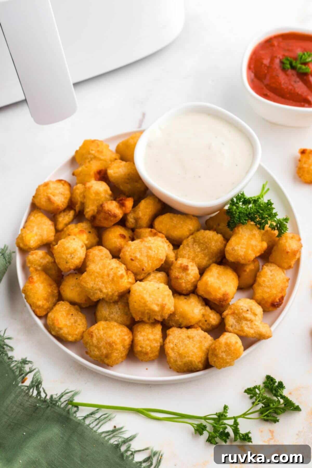 Crispy Air Fryer Frozen Cheese Curds 2 Golden brown crispy air fryer frozen cheese curds served on a white plate with a side of dipping sauce.
