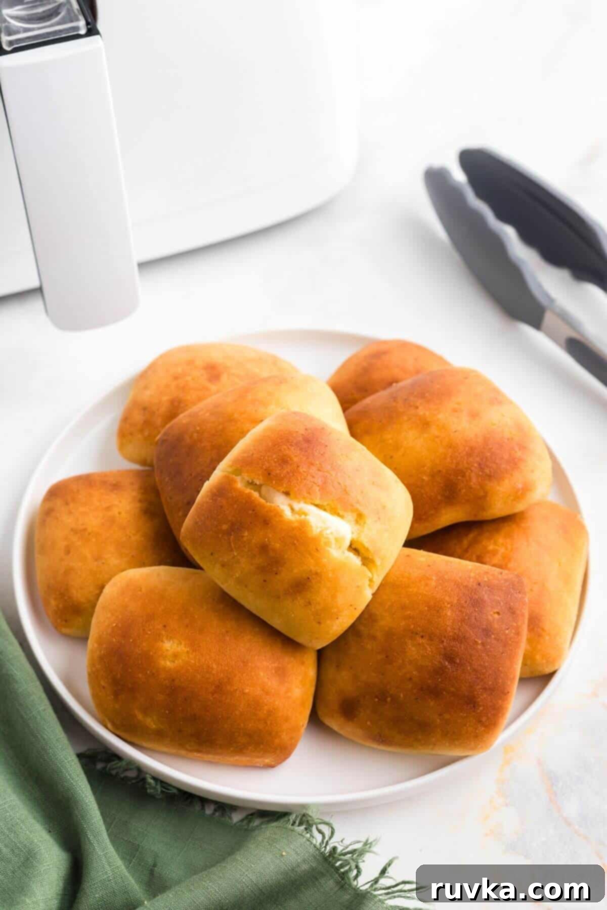 From Frozen to Fluffy: Air Fryer Dinner Rolls 2 Golden soft dinner rolls stacked on a white plate with one sliced and buttered.