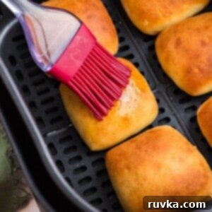 From Frozen to Fluffy: Air Fryer Dinner Rolls 7 Golden brown dinner rolls being brushed with melted butter in the air fryer basket.