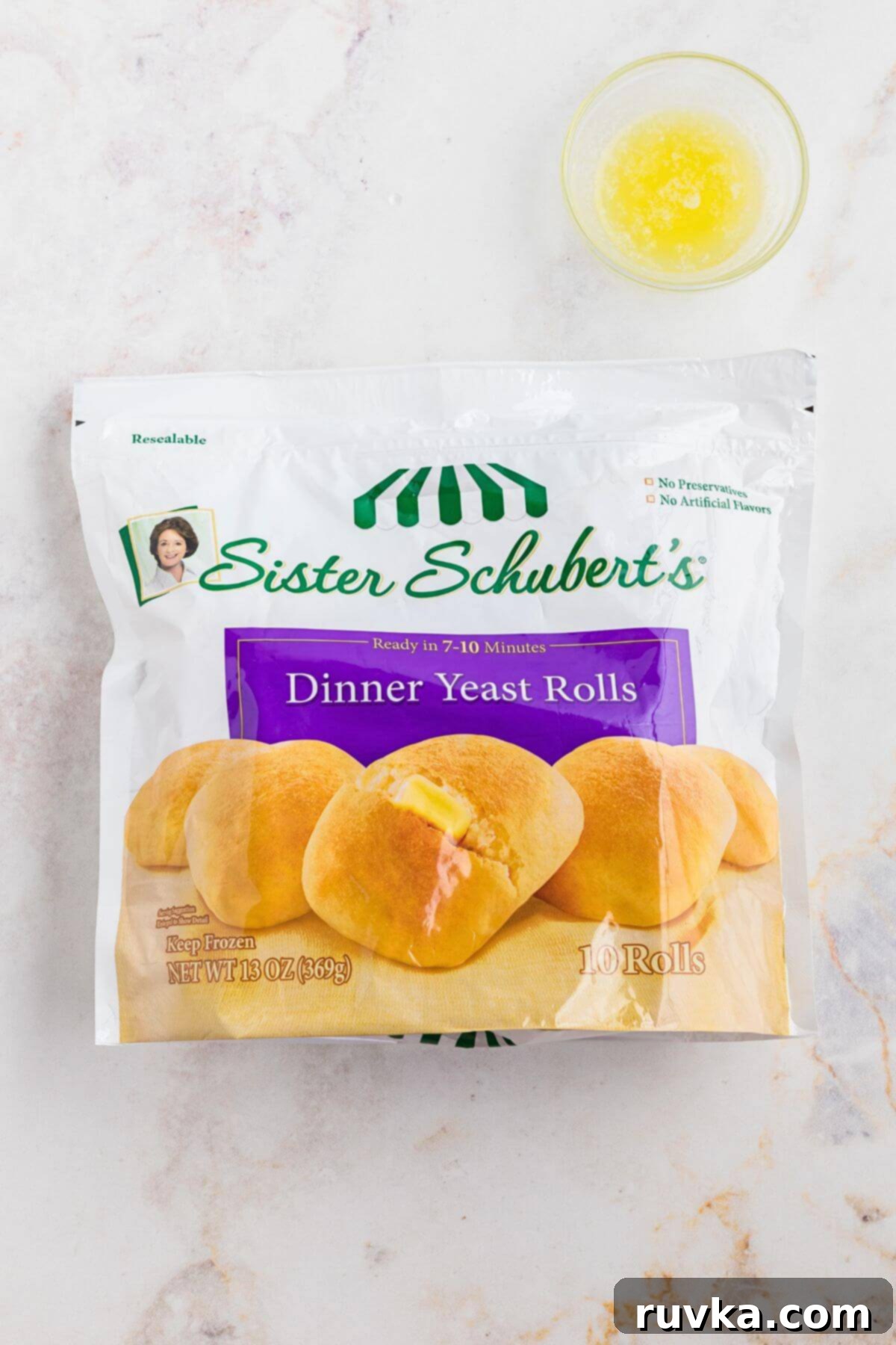 From Frozen to Fluffy: Air Fryer Dinner Rolls 3 Package of Sister Schubert's dinner yeast rolls on a marble table with a small bowl of melted butter.