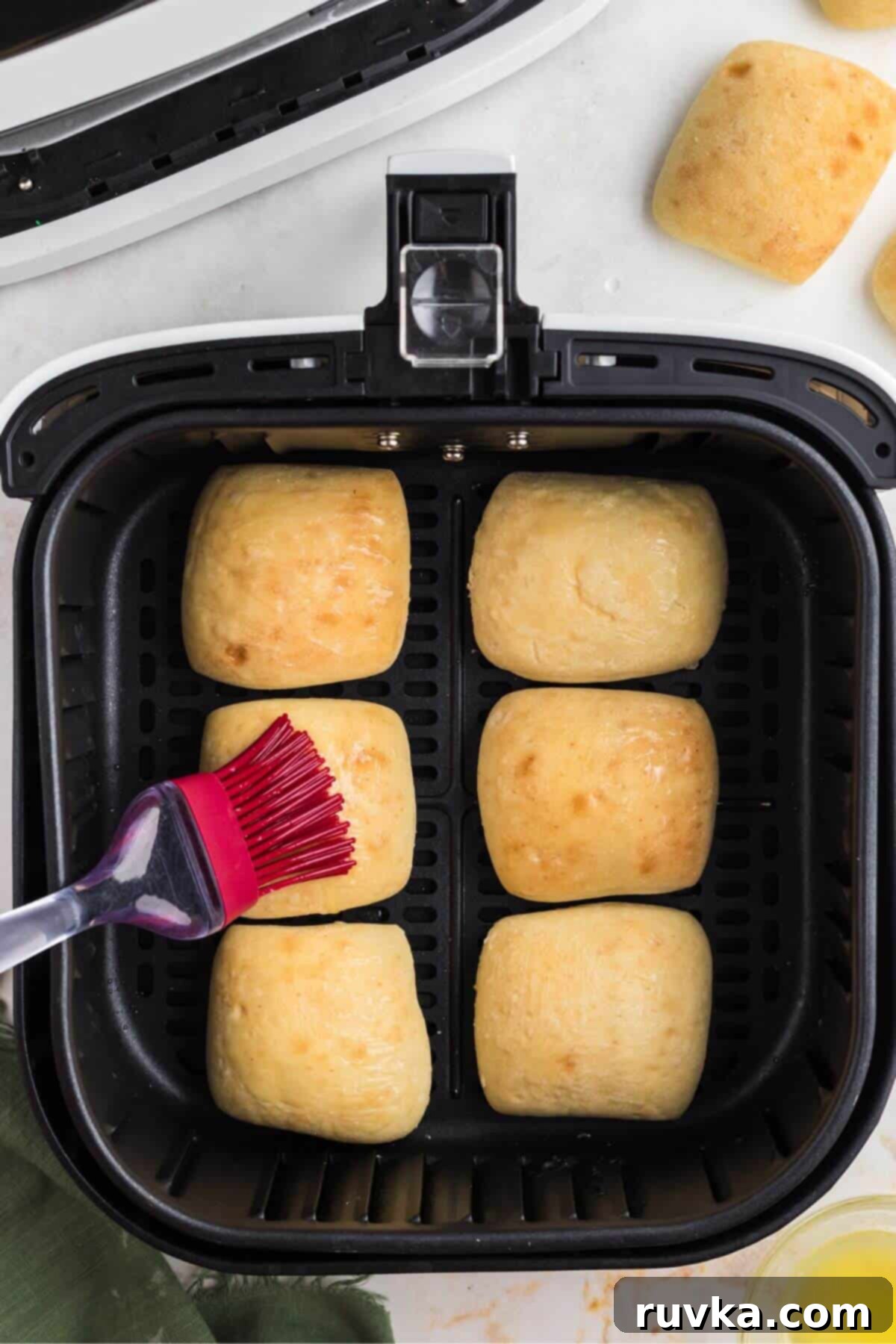 From Frozen to Fluffy: Air Fryer Dinner Rolls 4 Melted butter being brushed on frozen rolls in the air fryer basket.