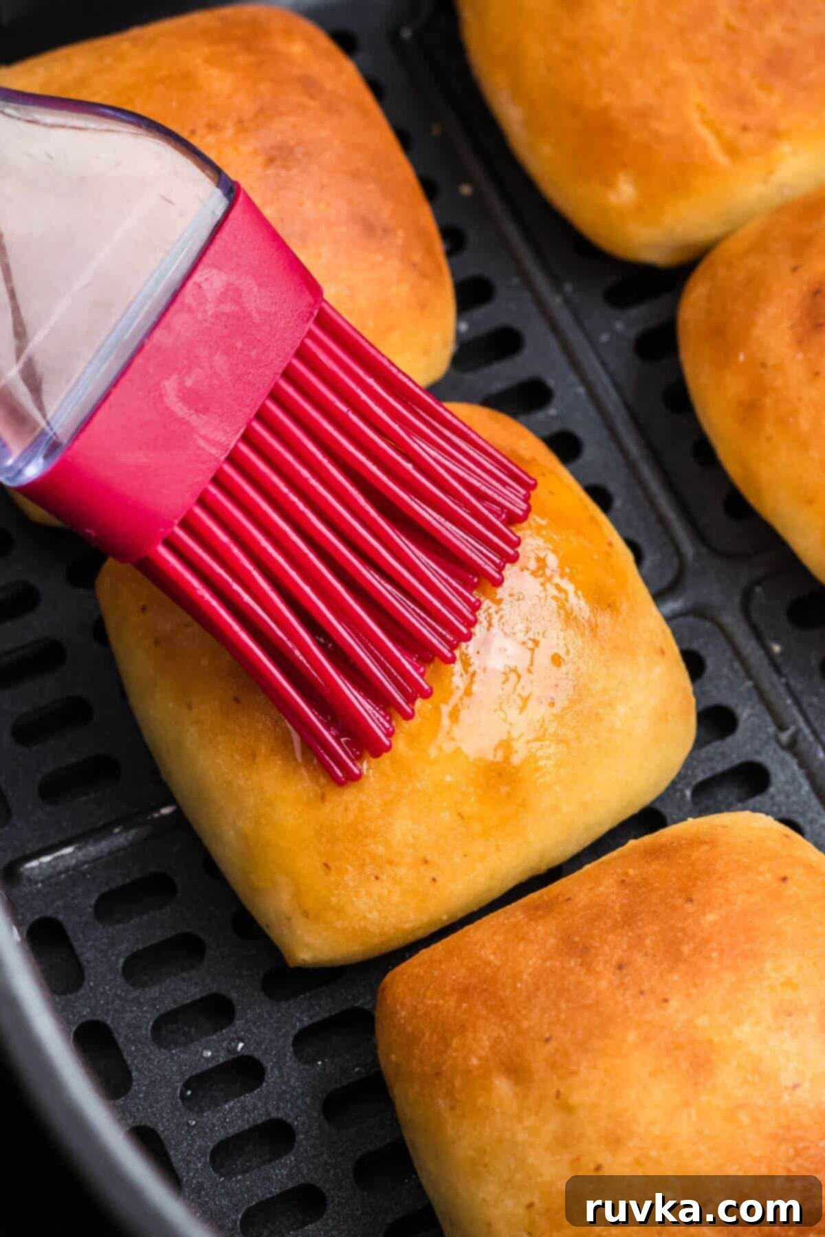 From Frozen to Fluffy: Air Fryer Dinner Rolls 6 Melted butter being brushed onto dinner rolls in the air fryer basket.