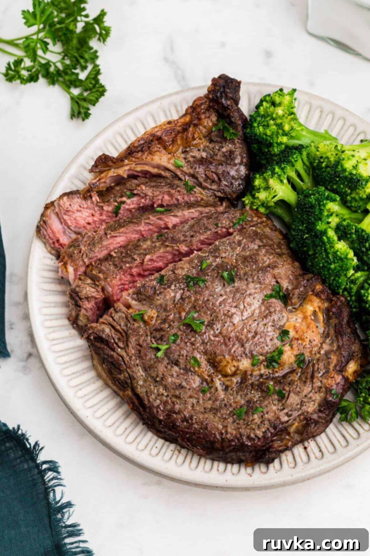 No Thaw Air Fryer Steak Perfection 6 Juicy seasoned steak sliced and served with broccoli on a white plate.