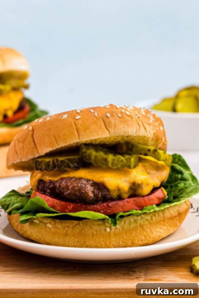 Perfect Air Fryer Burgers 2 Juicy hamburger with melted cheese, pickles, tomato and lettuce on a small white plate.