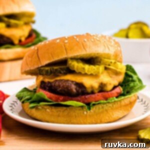 Perfect Air Fryer Burgers 8 Juicy hamburger topped with cheese, lettuce, tomato and pickles, on a bun.
