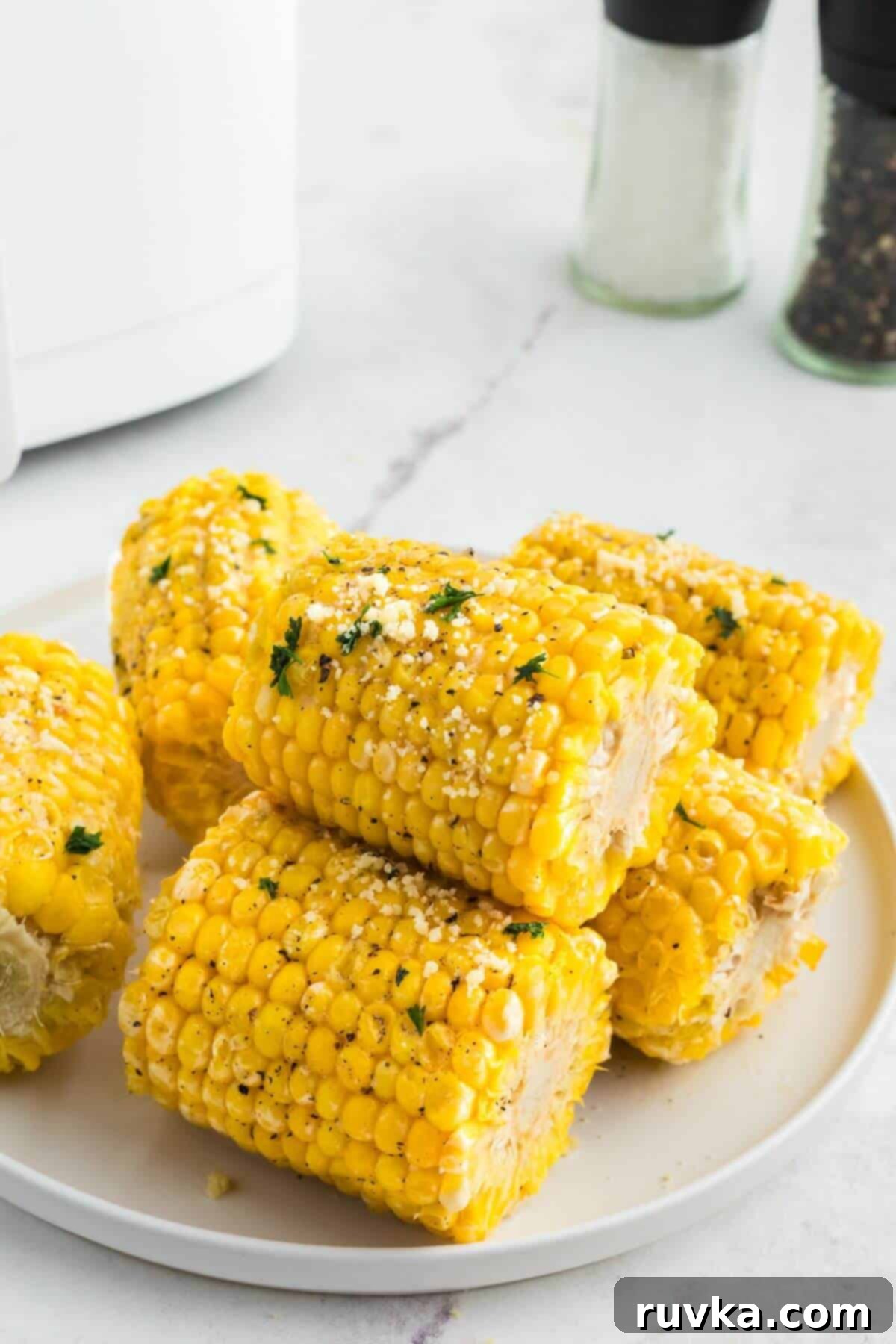 Perfect Air Fryer Frozen Corn on the Cob 2 Golden yellow ears of corn stacked on a white plate garnished with parsley flakes.