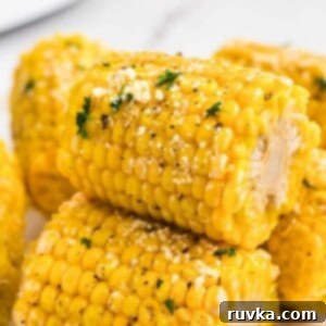 Perfect Air Fryer Frozen Corn on the Cob 7 Golden yellow ears of corn stacked and garnished with parmesan cheese and parsley flakes.