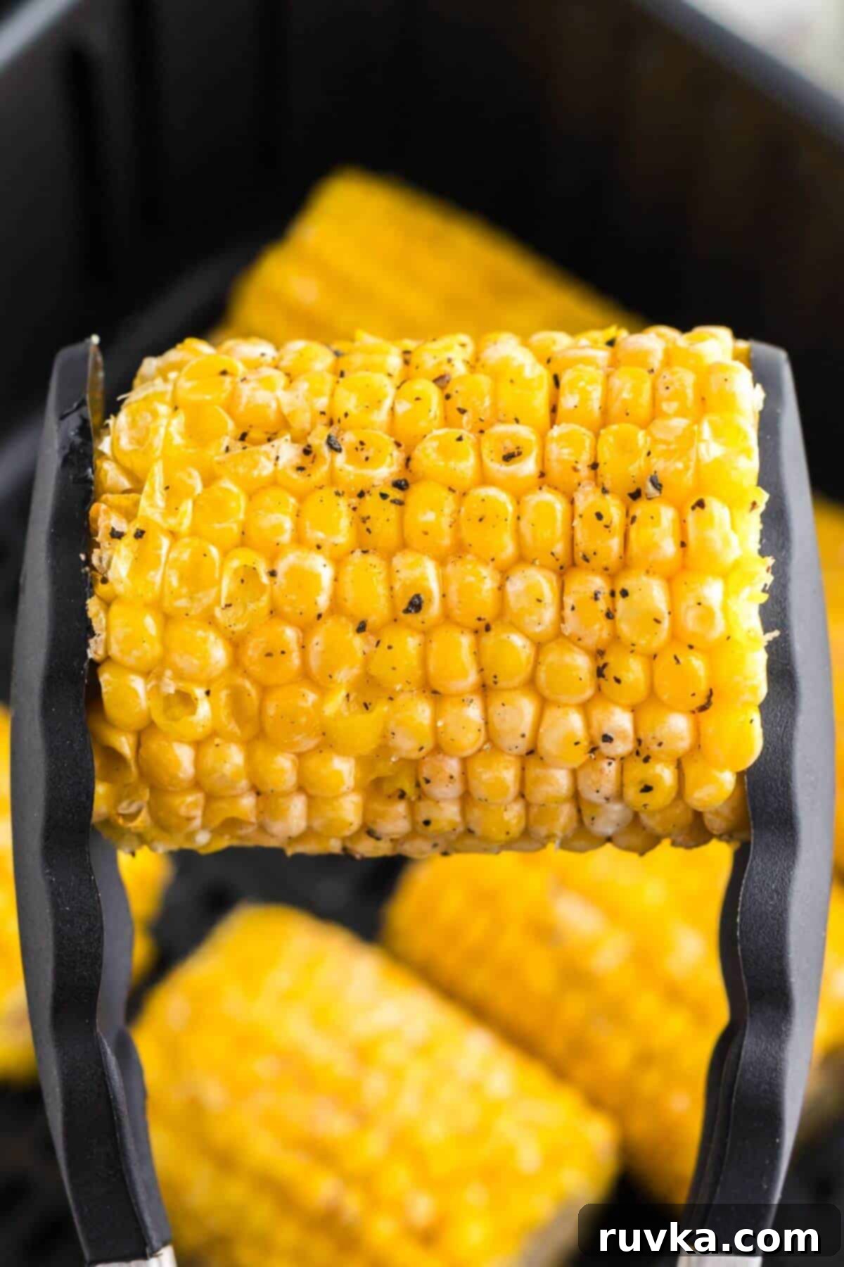 Perfect Air Fryer Frozen Corn on the Cob 6 Cooked yellow corn on the cob being held with tongs and seasoned.