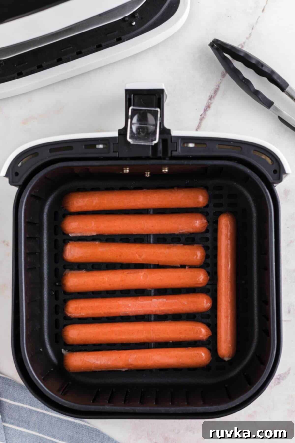Easy Air Fryer Frozen Hot Dogs 4 Uncooked frozen hot dogs in the air fryer basked before being cooked.