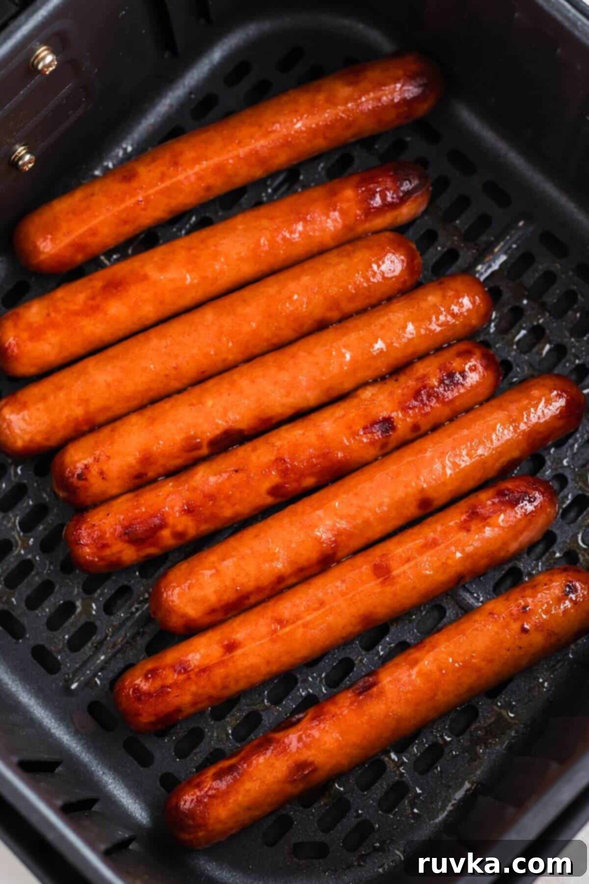 Easy Air Fryer Frozen Hot Dogs 5 Juicy cooked hot dogs in the air fryer basket after being cooked.