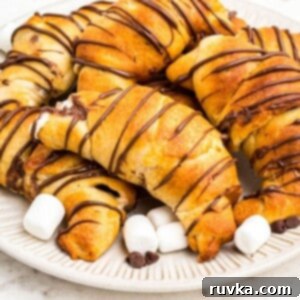 Air Fryer S'mores Crescent Rolls 9 Golden air fryer s'mores crescent rolls stacked on a plate with mini marshmallows and chocolate chips, stacked on a plate.