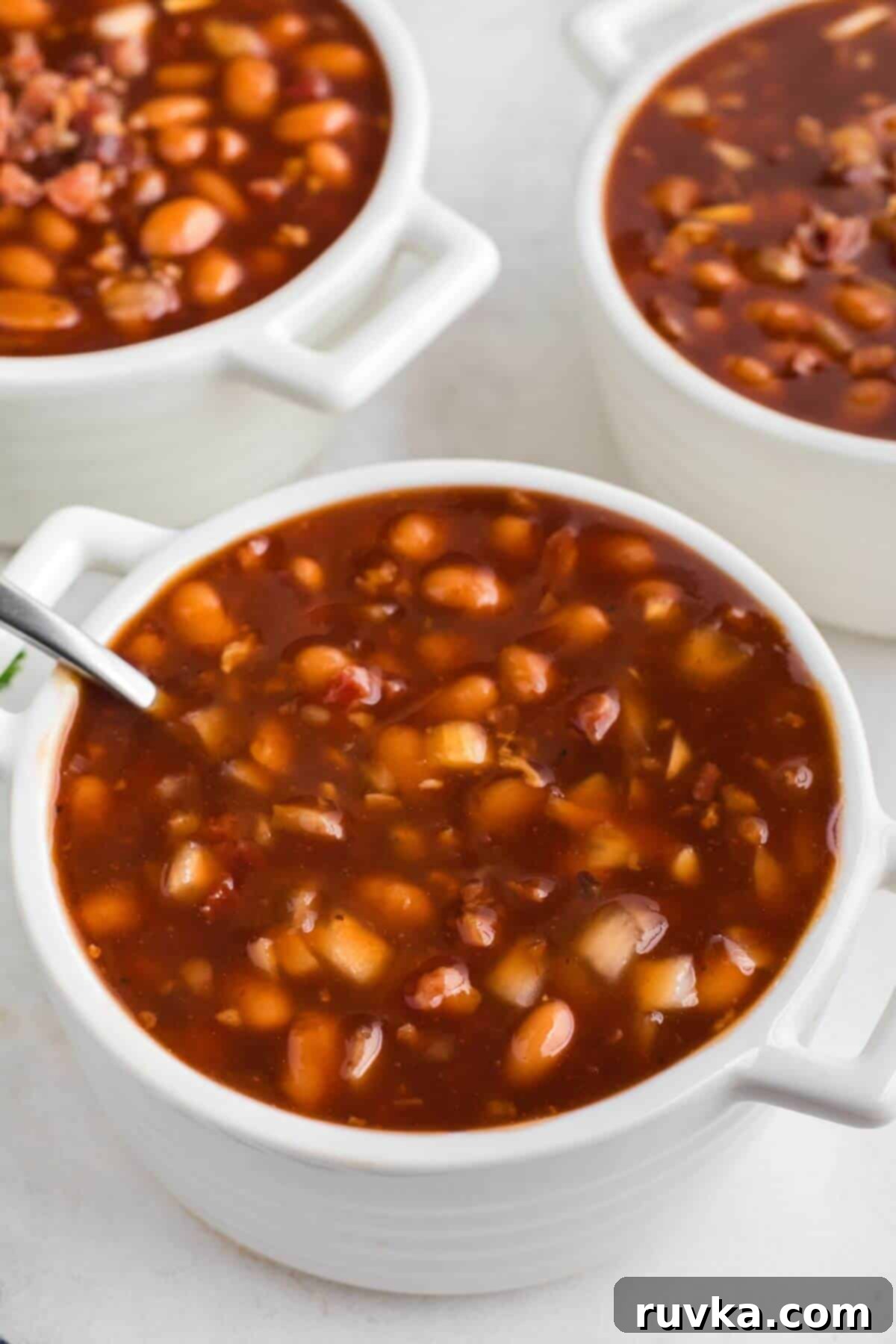 Perfect Air Fryer Baked Beans 2 Juicy brown baked beans in white bowls with a spoon on the side.
