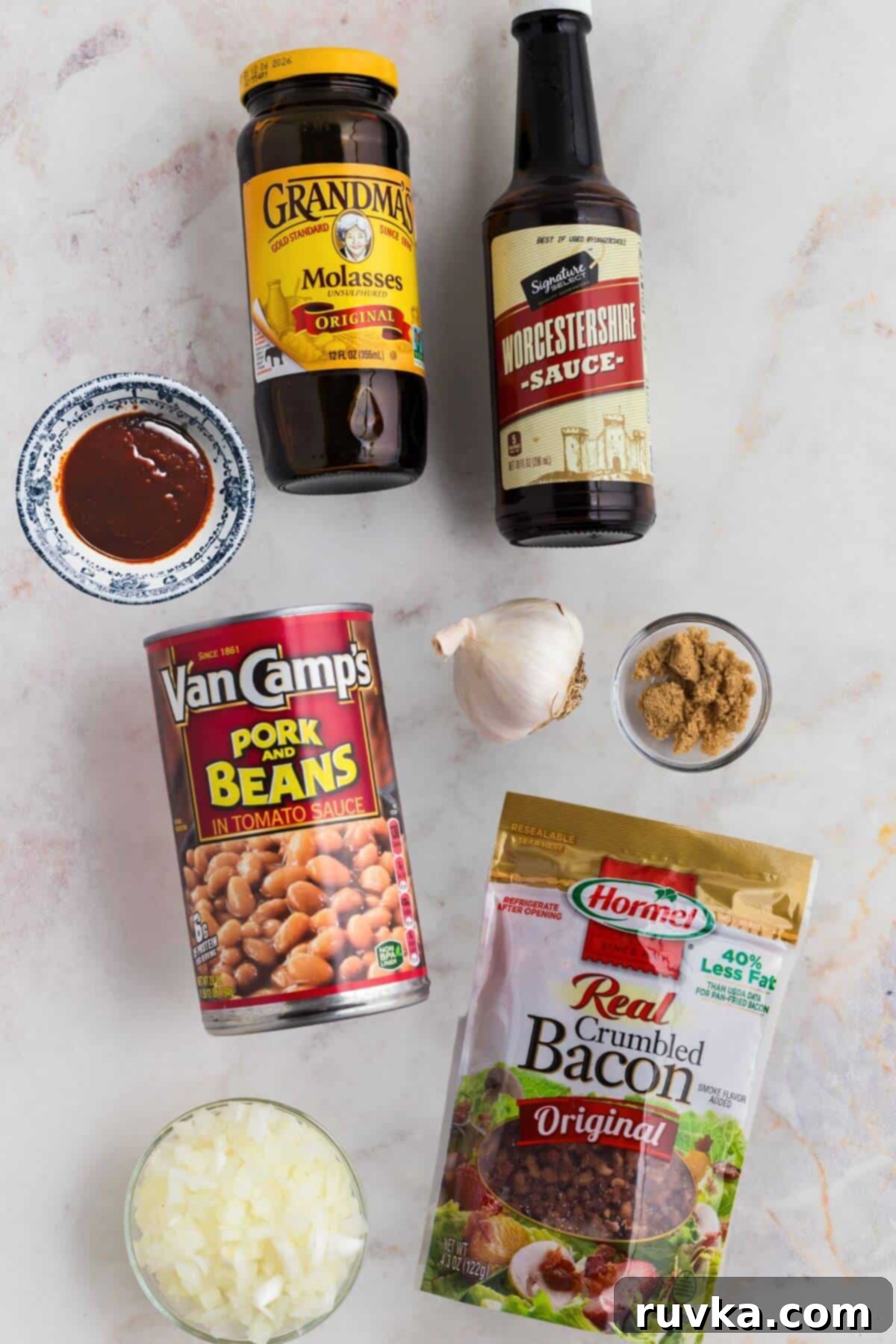 Perfect Air Fryer Baked Beans 3 Ingredients of molasses, pork and beans, chopped onions, crumbled bacon, and more, needed to make baked beans from scratch on a marble table.