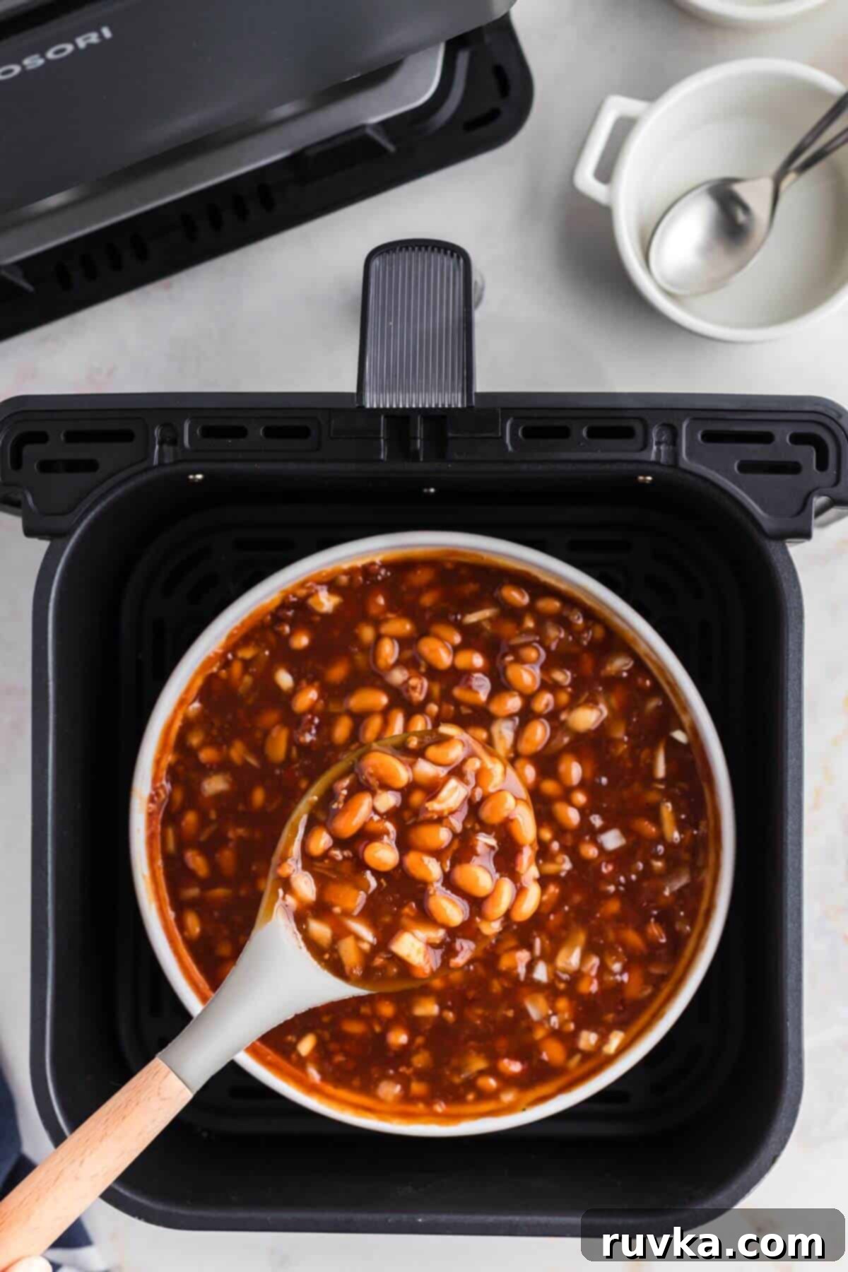 Perfect Air Fryer Baked Beans 6 Juicy baked beans after being cooked in the air fryer, being scooped with a spoon.