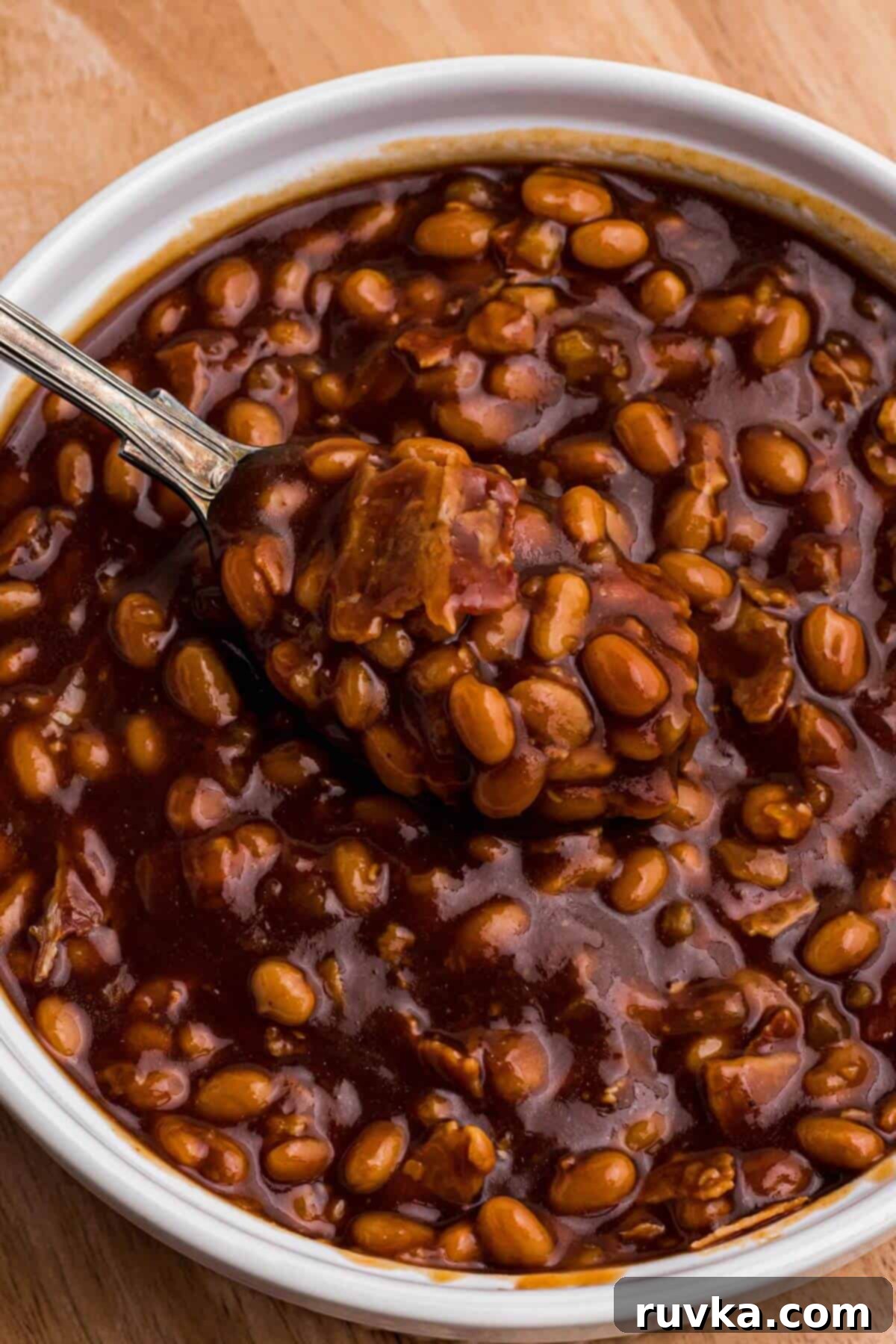 Perfect Air Fryer Baked Beans 7 Juicy golden brown baked beans being scooped up with a spoon topped with bacon crumbles.
