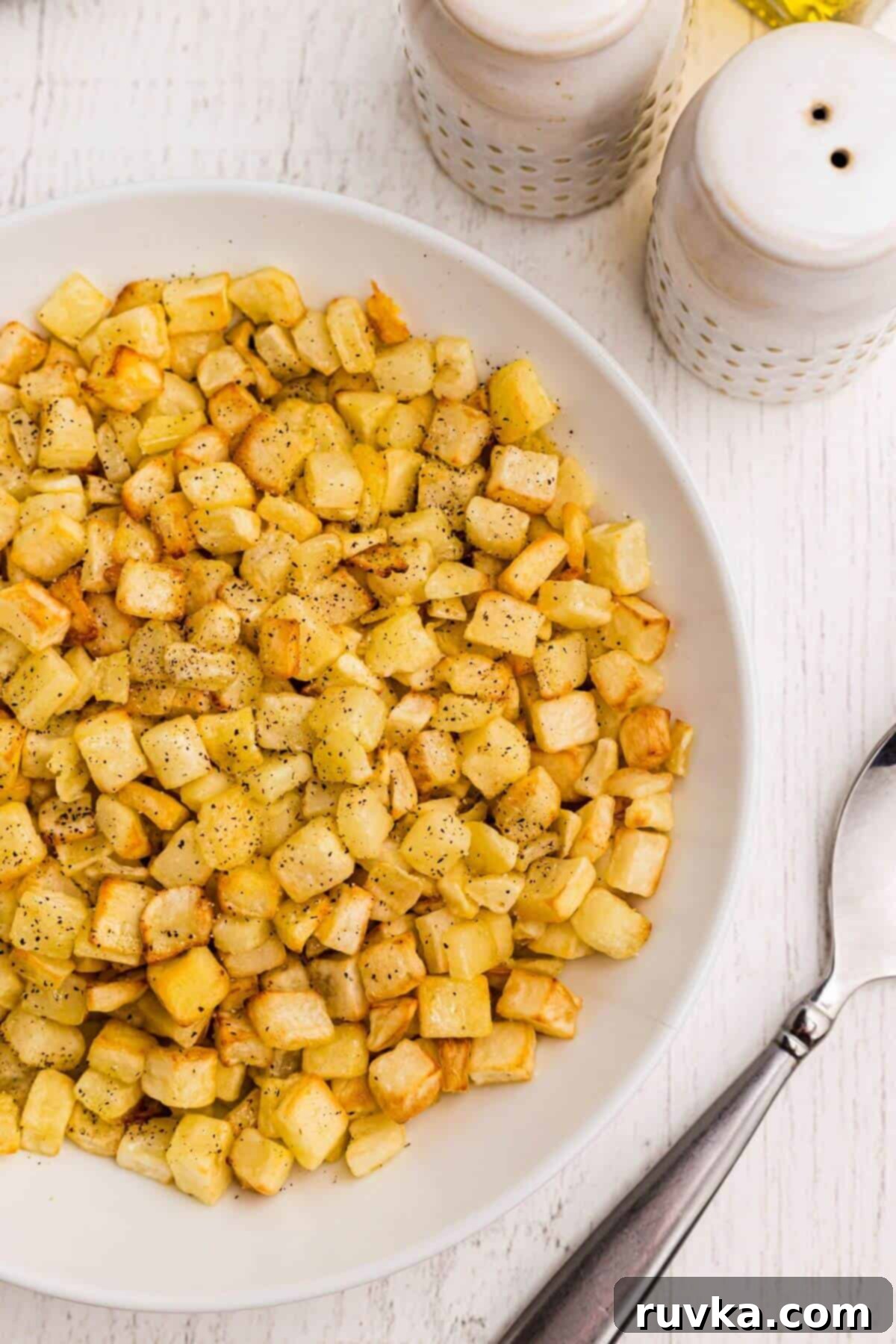 Crispy Air Fryer Frozen Potatoes 2 Golden seasoned diced potatoes in a white bowl with a serving spoon.