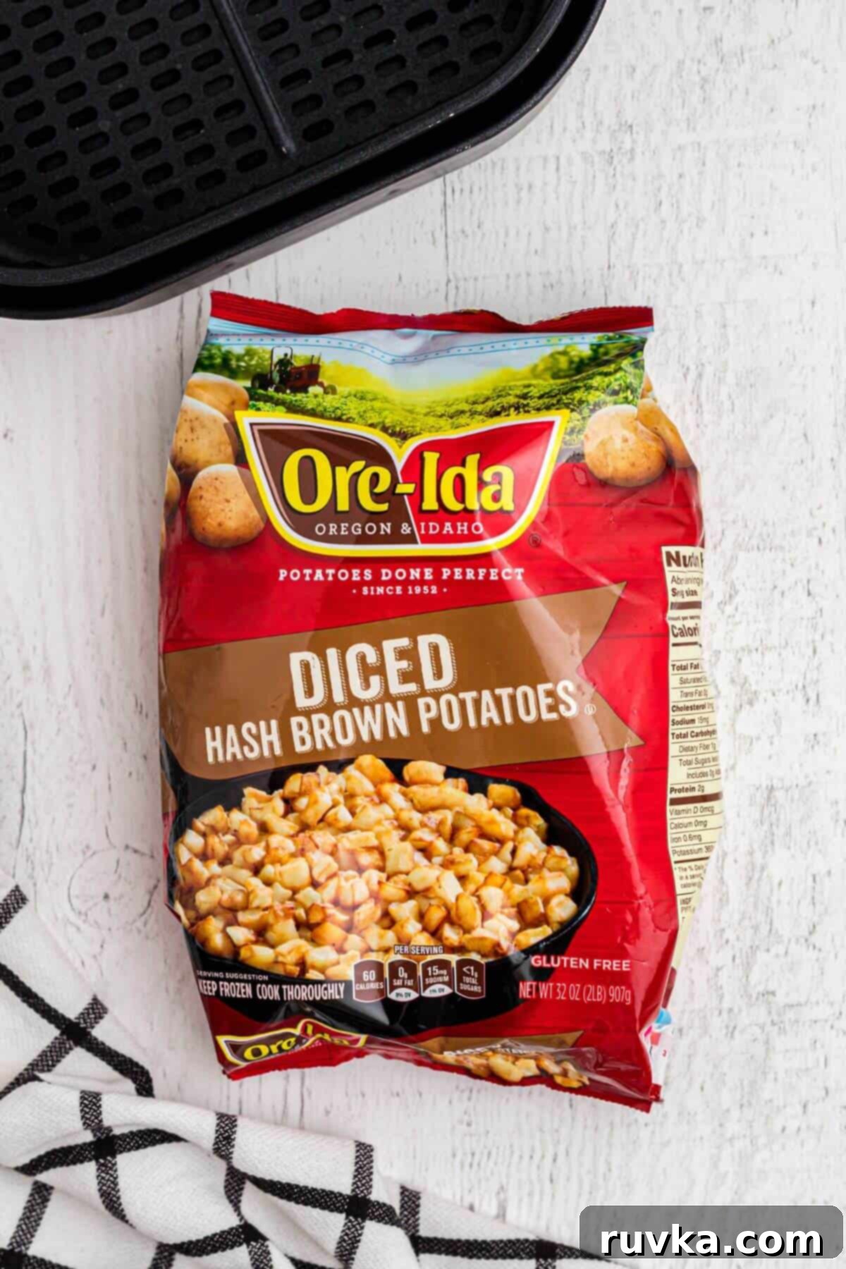 Crispy Air Fryer Frozen Potatoes 3 One bag of frozen diced potatoes in front of an air fryer basket.