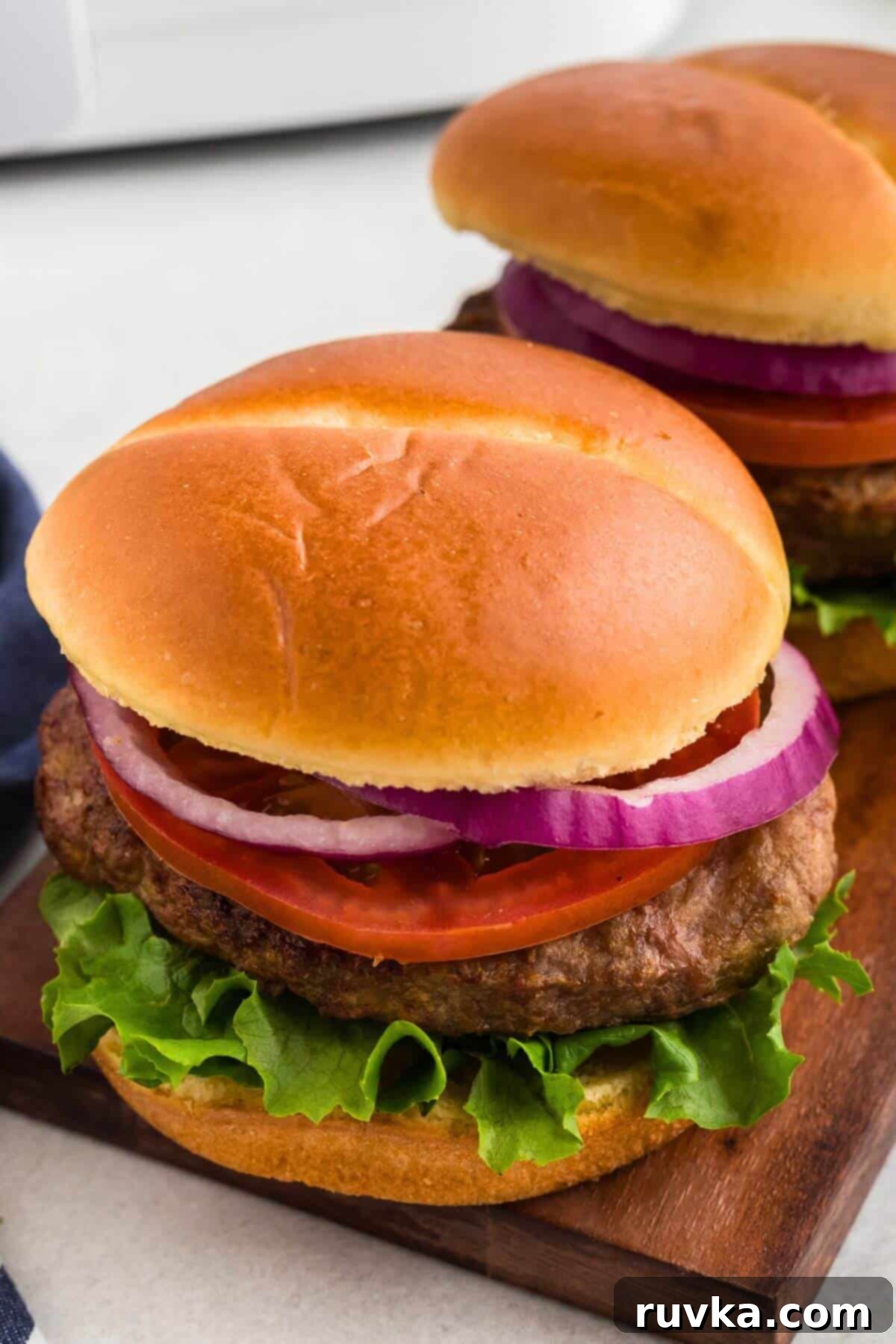 Perfect Air Fryer Frozen Turkey Burgers 2 Juicy turkey burger in a bun with fresh lettuce, ripe tomato slices, and crisp onion rings, presented on a rustic wooden cutting board.