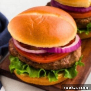 Perfect Air Fryer Frozen Turkey Burgers 8 Juicy turkey burger in a bun with lettuce, tomato, and onion, on a wooden cutting board.
