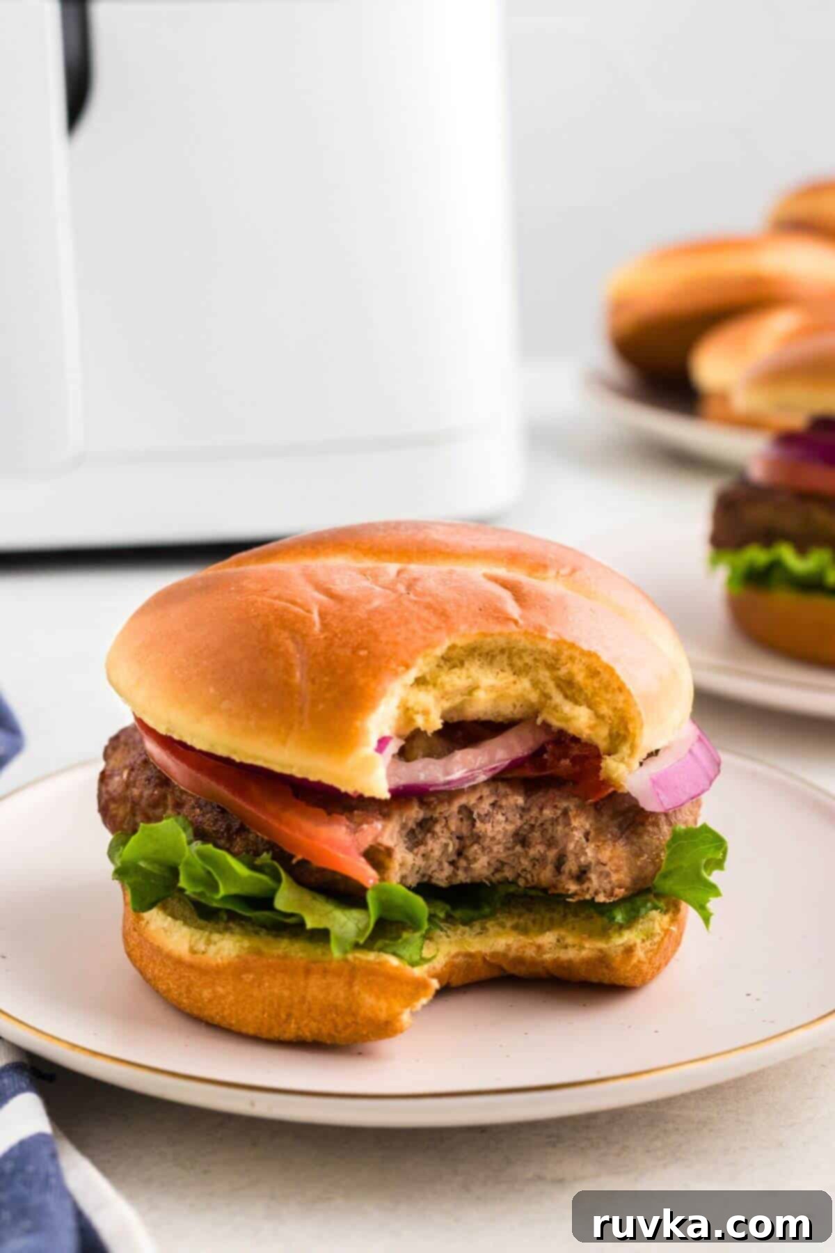 Perfect Air Fryer Frozen Turkey Burgers 6 Juicy turkey burger in a bun with lettuce, tomato, and onions, with a bite taken out, showing the tender patty inside.