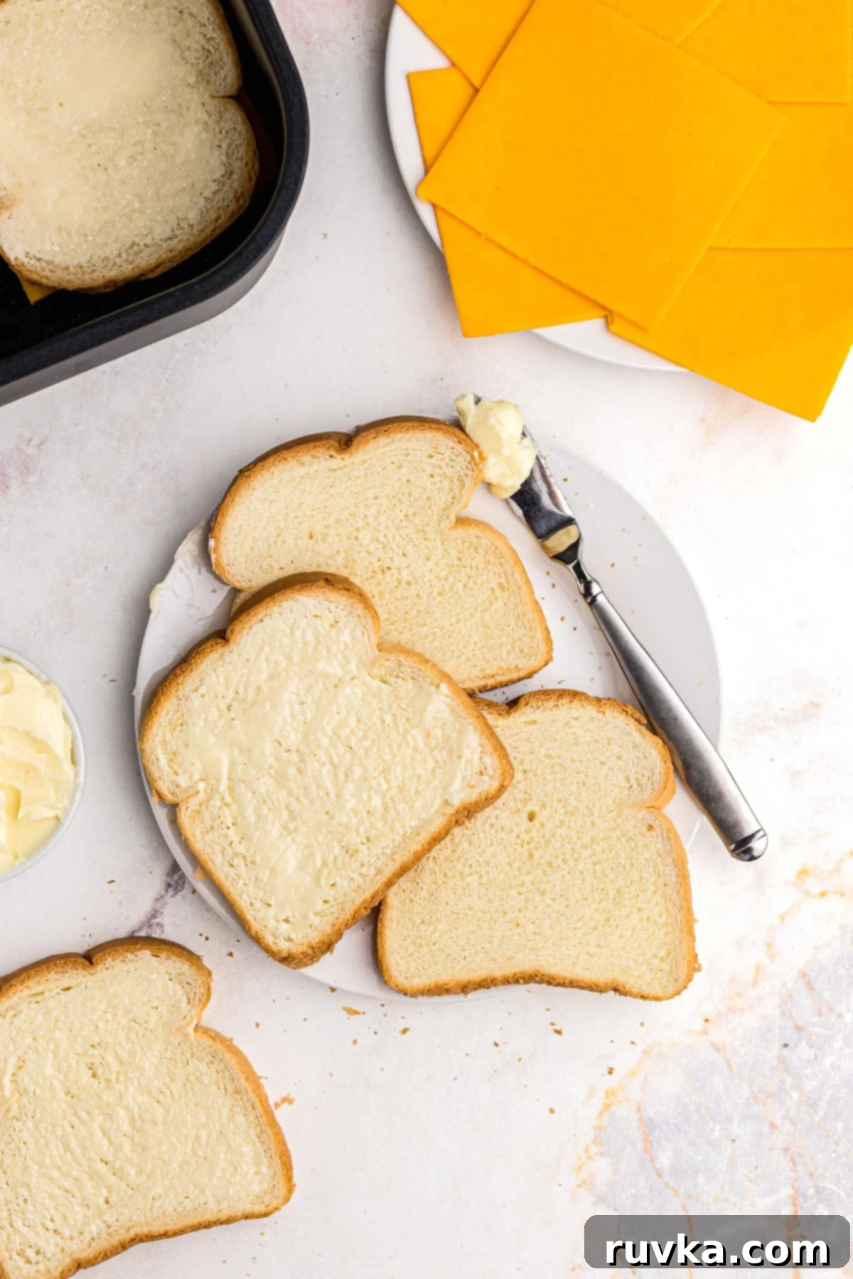 Golden and Gooey Air Fryer Grilled Cheese 4 Slices of bread being buttered, then topped with slice of cheese, placed in the air fryer.