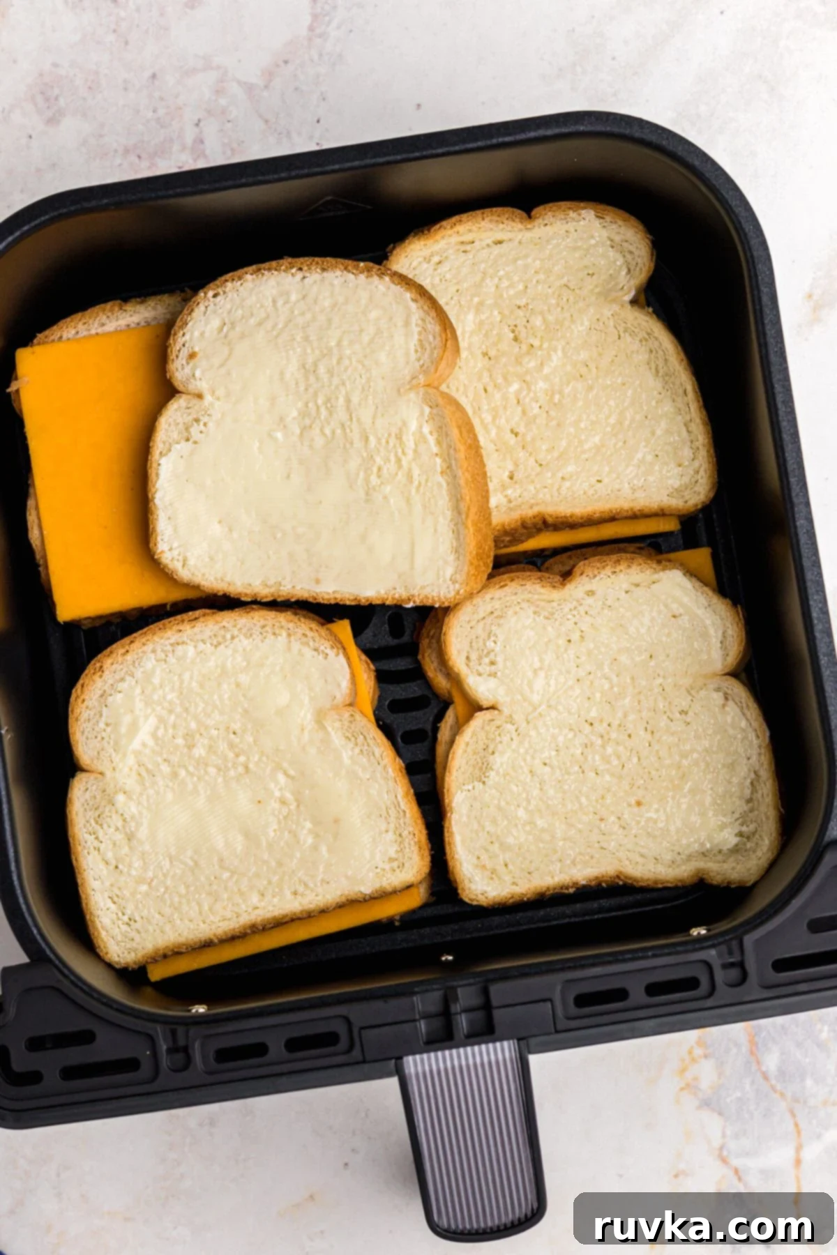 Golden and Gooey Air Fryer Grilled Cheese 5 Bread slices with butter on one side, with a slice of cheese in the middle of bread slices, in the air fryer basket before being cooked.