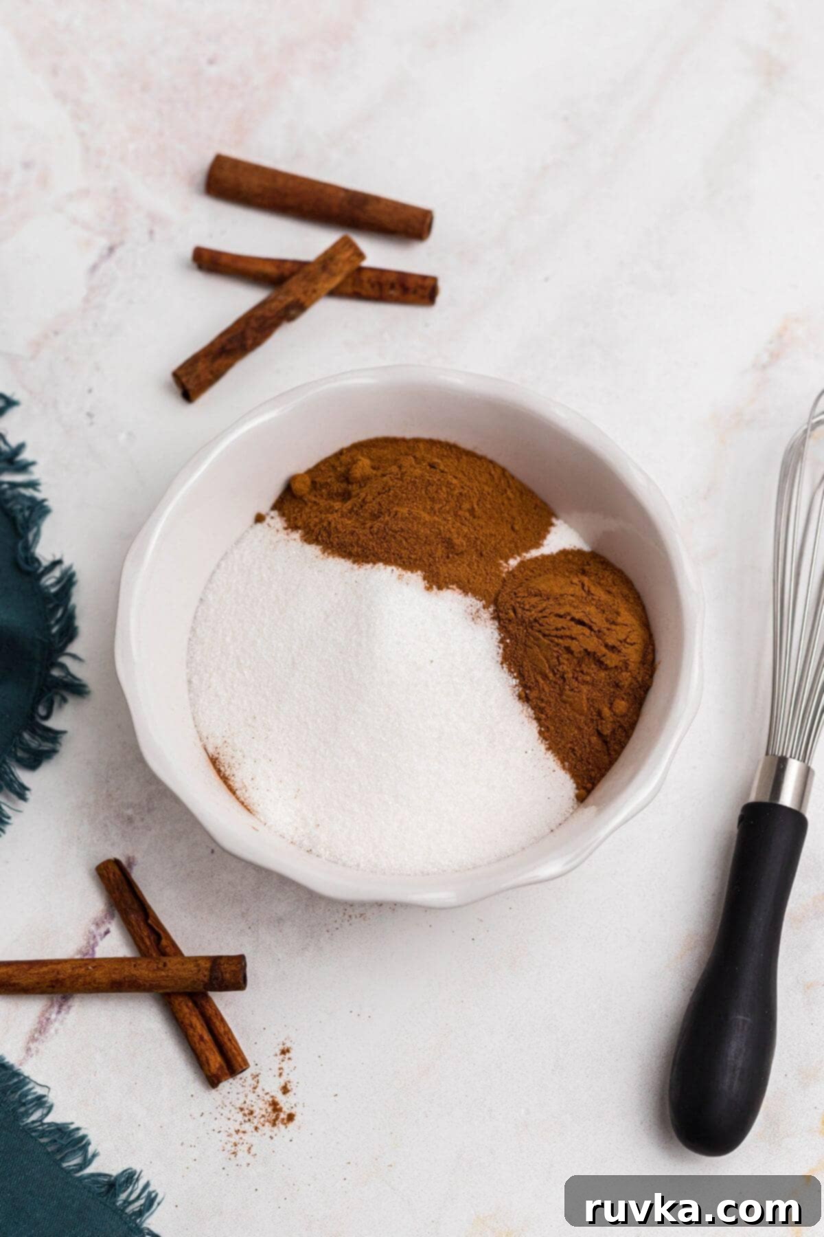 Spiced Sweetness 4 Cinnamon and sugar being mixed together in a small white bowl with a whisk on the table.