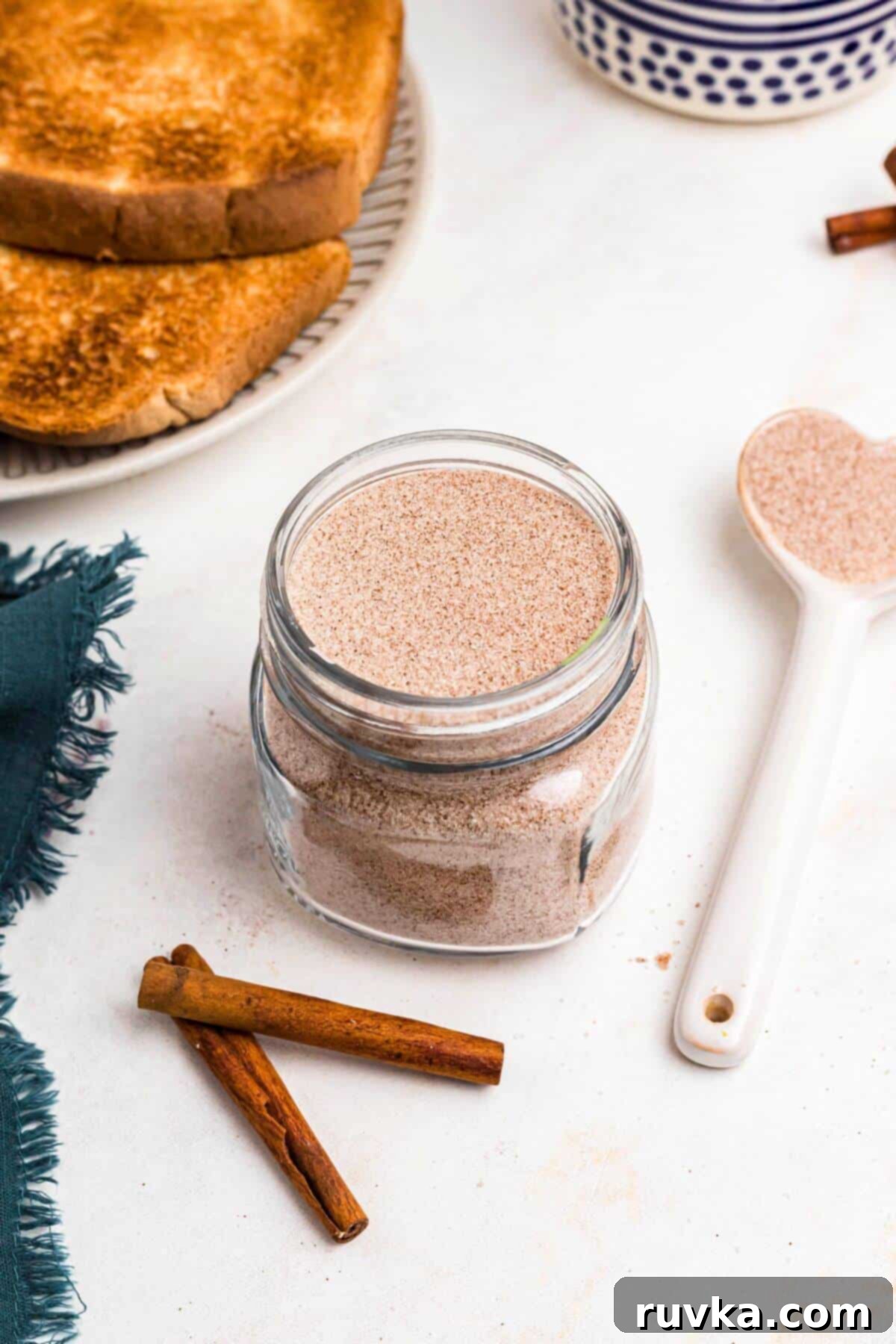 Spiced Sweetness 6 Cinnamon sugar mixture being stored in a clear glass jar in front of toast on a marble table.